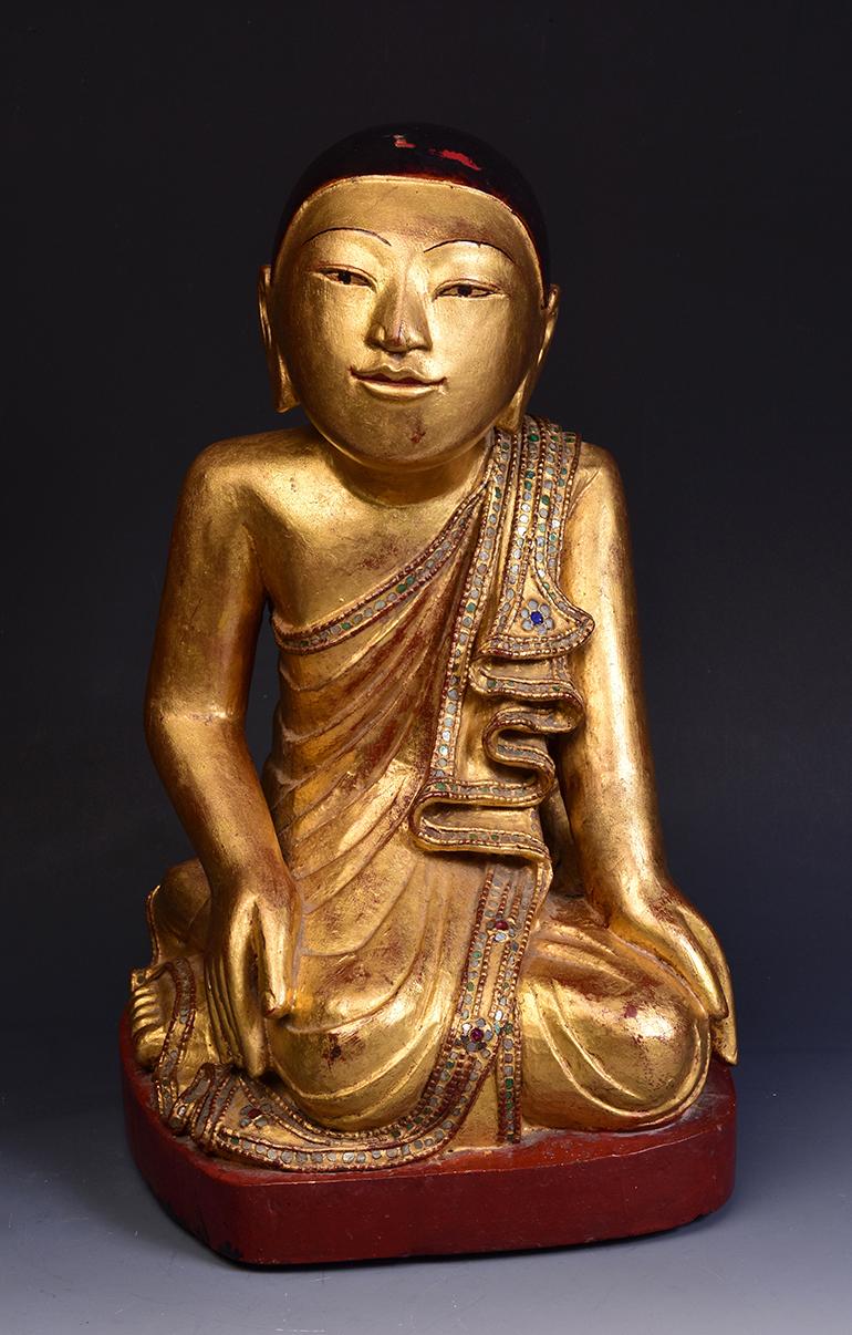 Burmese wooden disciple seated on a base, with gilded gold and inlay of colorful glass pieces on the borders of the robe.

Age: Burmese, 19th century
Size: Height 38 C.M. / Width 22 C.M. / Depth 23 C.M.
Condition: Nice condition overall (some