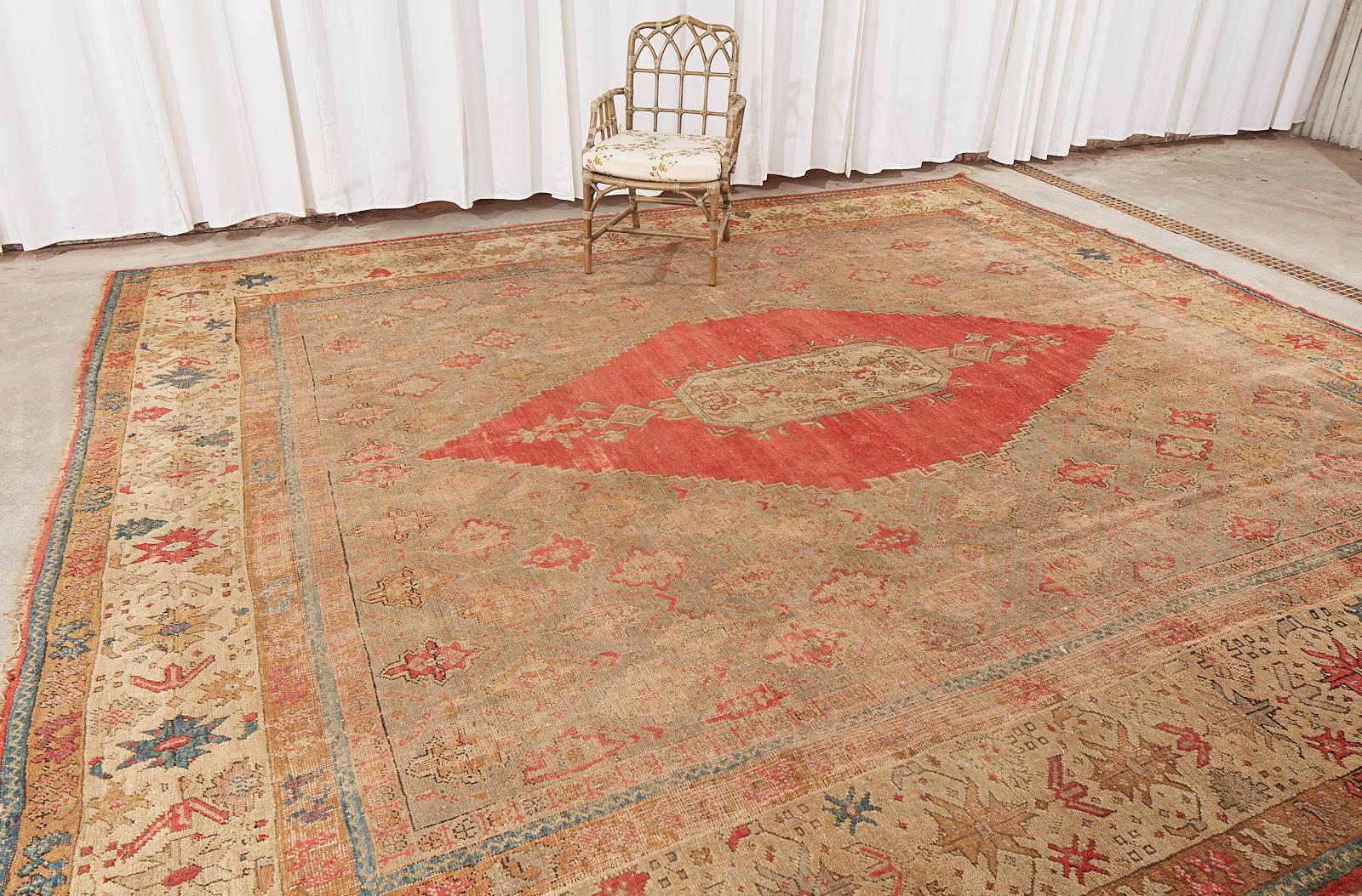 Dramatic late 19th century hand-knotted wool oushak rug featuring a rectangular center in a diamond shaped crimson red medallion. Aged, distressed patina with past alteration to make the current size in a near square shape.