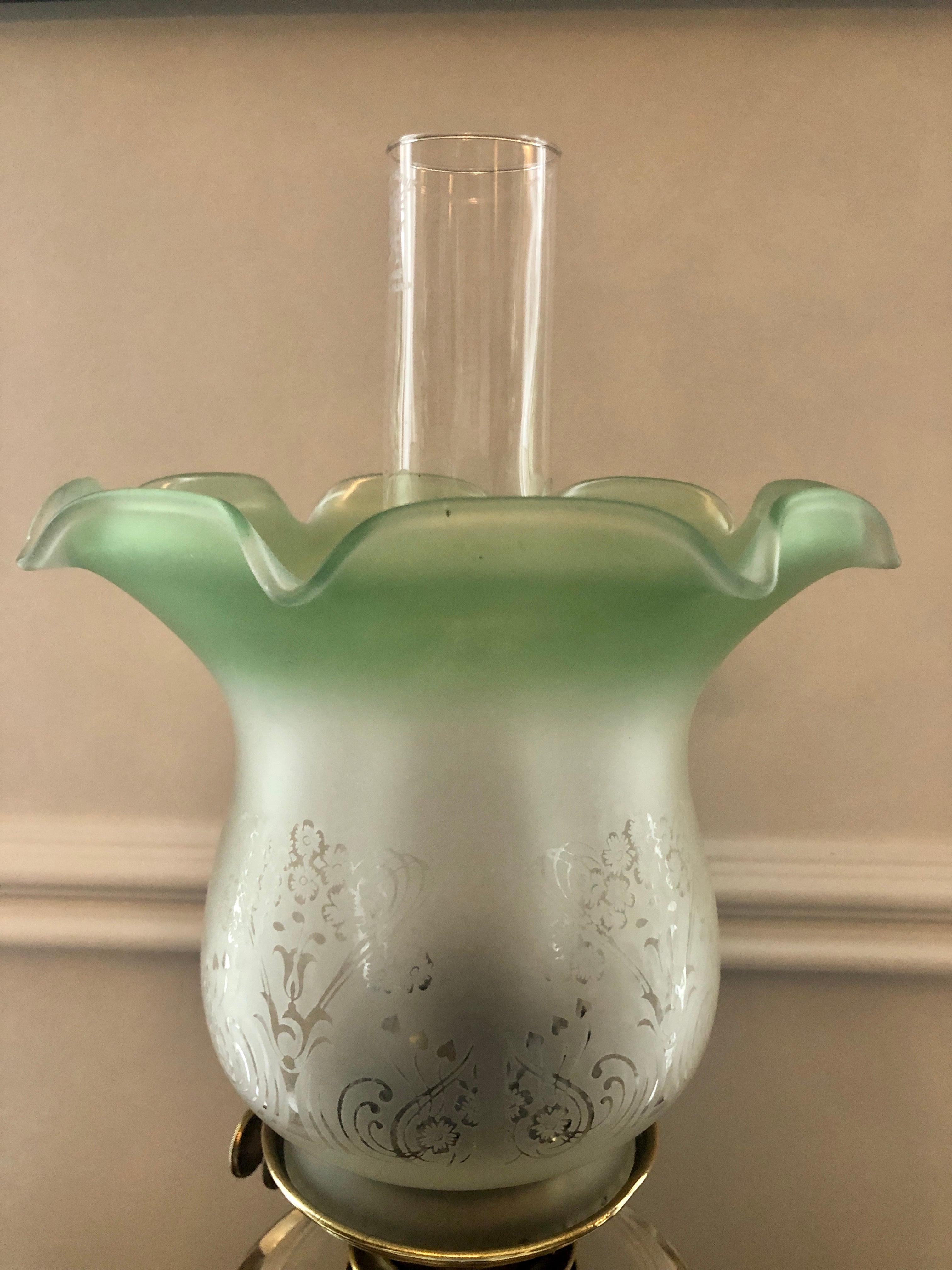 A 19th century Victorian brass oil lamp having a pretty tulip shaped white and green elegantly etched glass shade with a single burner stood on a round reeded brass base.


  