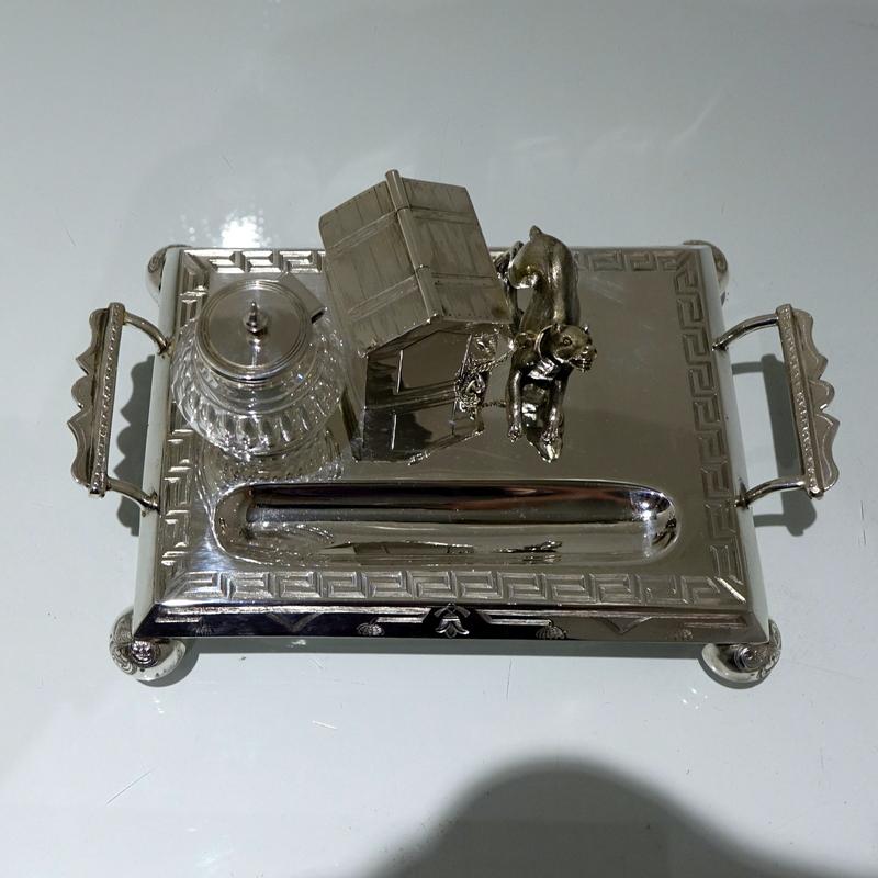 A splendid rectangular silver plated novelty dog and kennel themed inkstand. The outer border of the base has stylish “Greek key” engraving. The bulbous circular hinged ink bottle has ornate oval cutting.

 

Measures: Length 9
