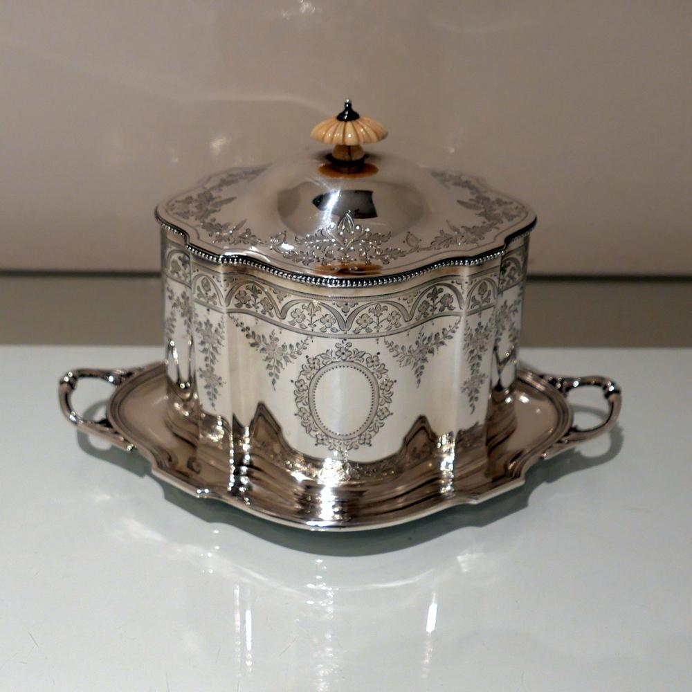 A very rare model of a shaped oval Victorian silver biscuit box mounted on a contemporary two handled under tray. The box is decorated with an upper band of bright cut engraving and elegant oval central cartouches. The domed lid is hinged and has an