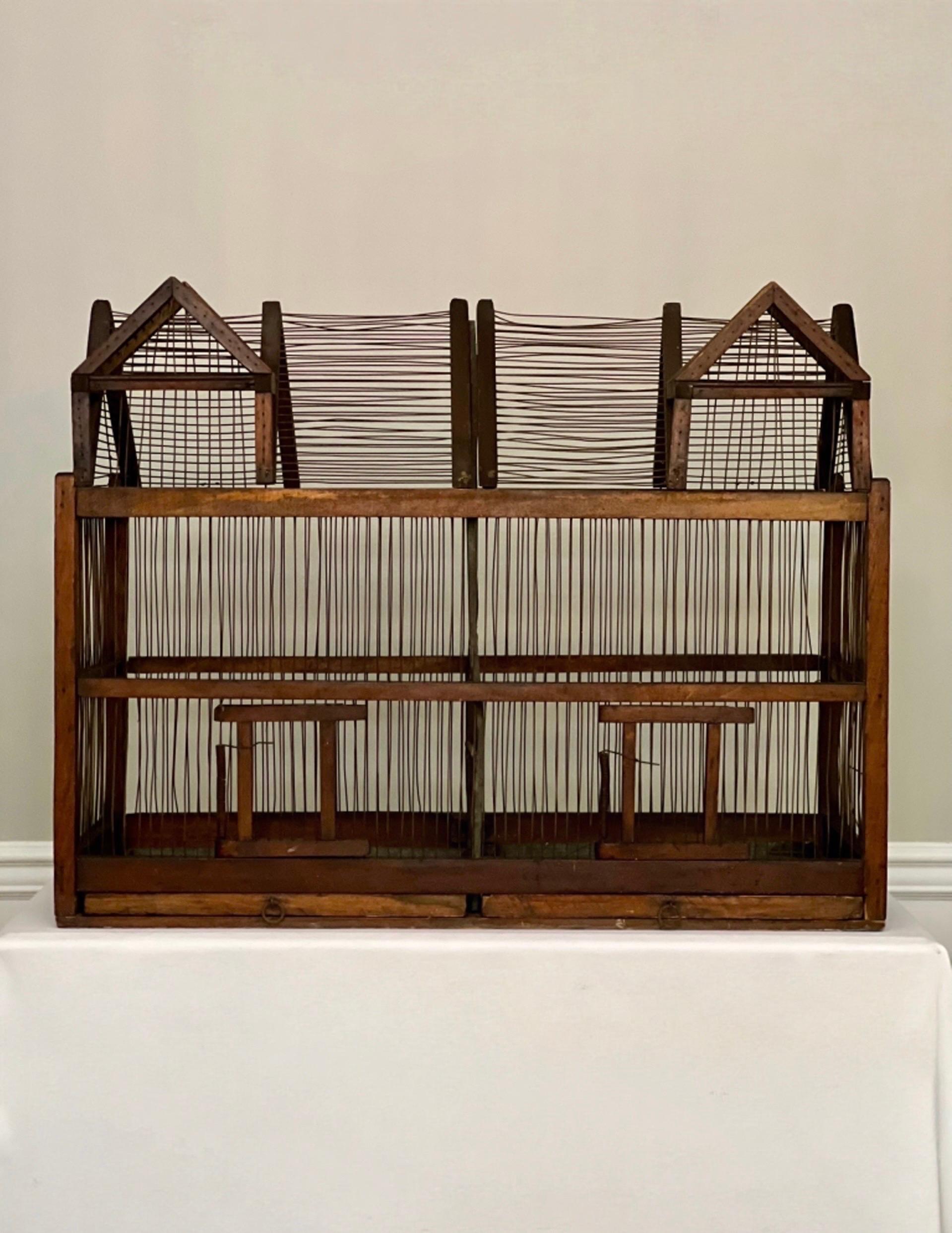 Ancienne cage à oiseaux architecturale en bois et en fil de fer à deux compartiments, vers 1890.  La cabane à oiseaux comprend des compartiments divisés côte à côte, chacun doté d'une porte à ressort et d'une troisième porte mutuelle, d'un toit à