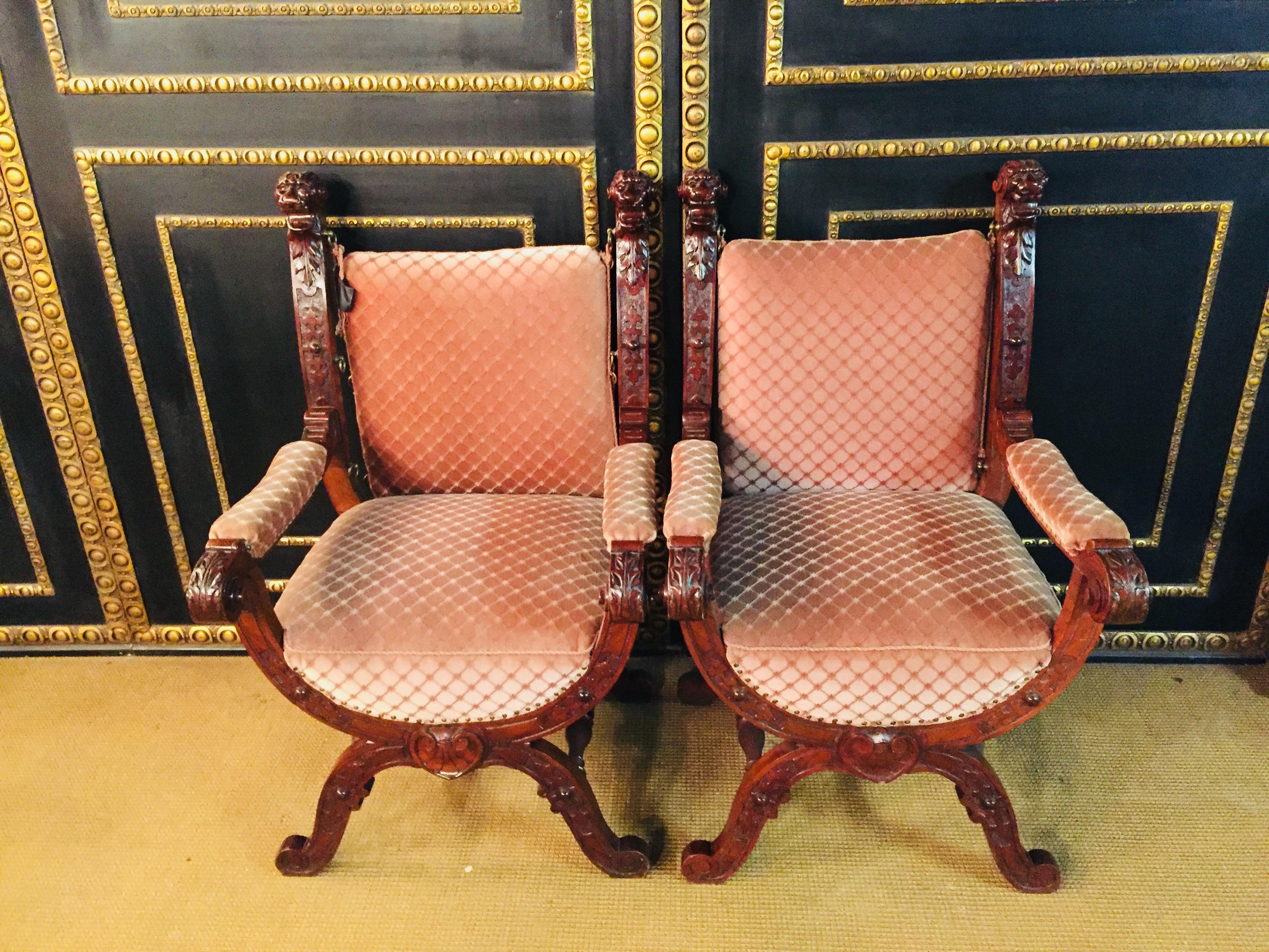 19th century 2 Armchairs solid walnut, all-round carved with historicism ornaments, backrest each side crowned by lion's heads with wide open mouth, scissor legs with baluster crossbars, backrest, upholstered seat and armrests.