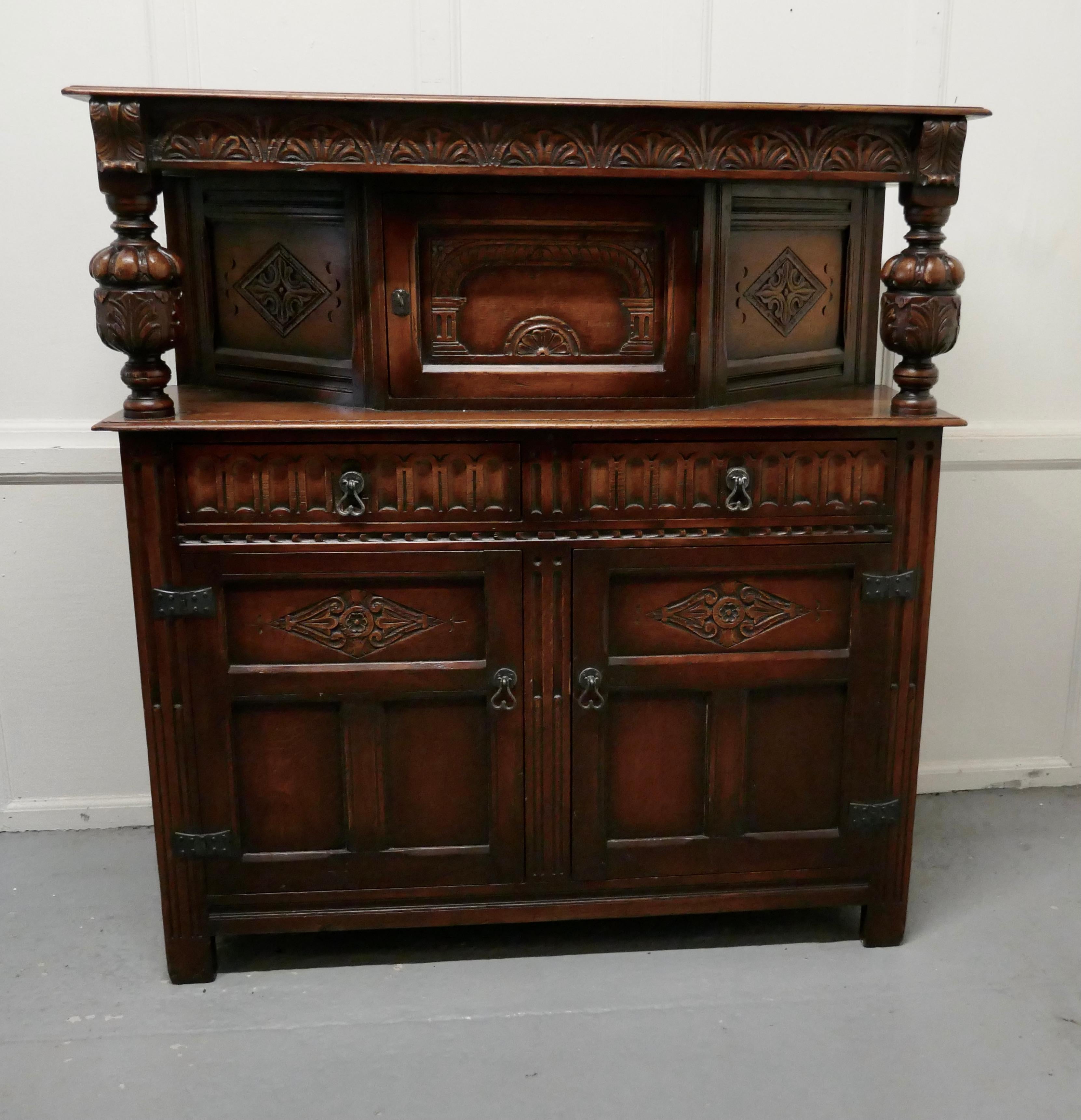 19th century Arts & Crafts Gothic carved oak court cupboard

This is a very attractive piece of carved oak furniture, the top section has a long cupboard enclosed with a carved panels and door in the centre
On each side there is a chunky carved