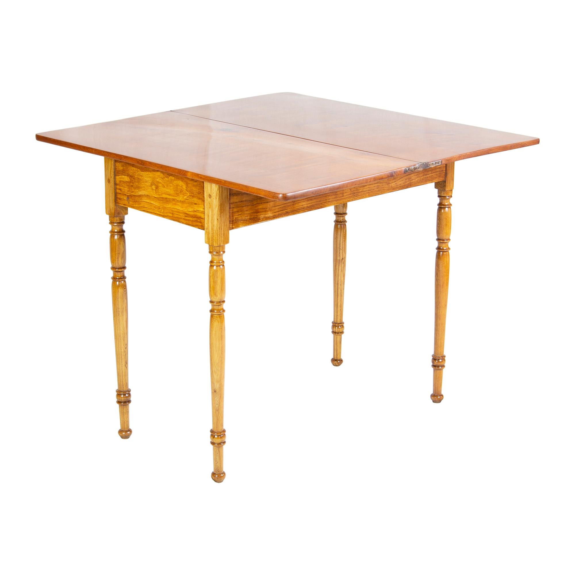 Kleiner Spiel- oder Konsolentisch aus Eschenholz. Der Tisch stammt aus der Zeit des späten Biedermeiers um 1850. Die Tischplatte kann um 90° gedreht und damit aufgeklappt werden. Dadurch erhöht sich die Tiefe des Tisches von 42 cm auf 84 cm. Der