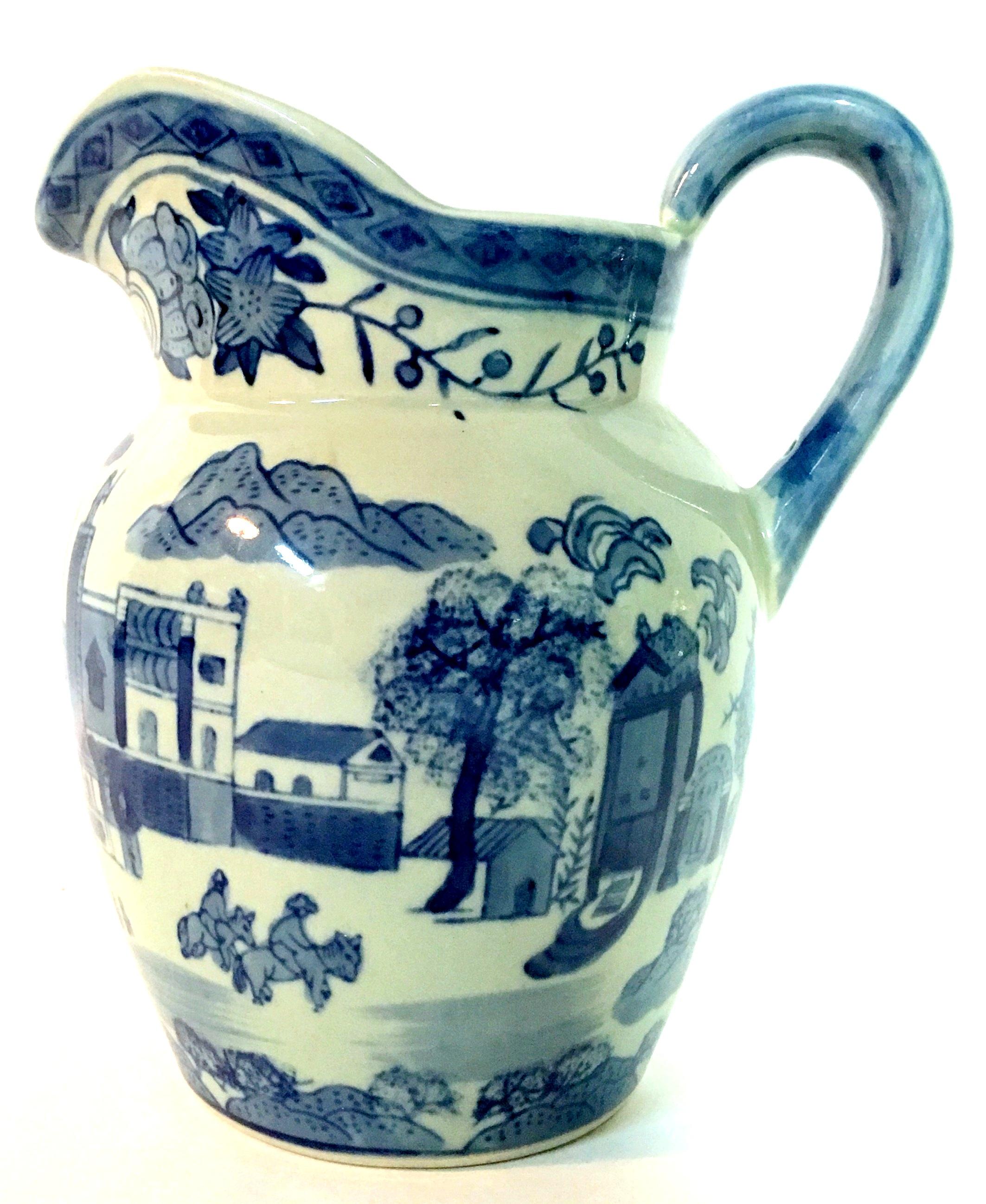 Antique Ceramic Glaze blue and white celadon handled beverage pitcher. Features a  village scene motif.  Makers Mark appears on underside.