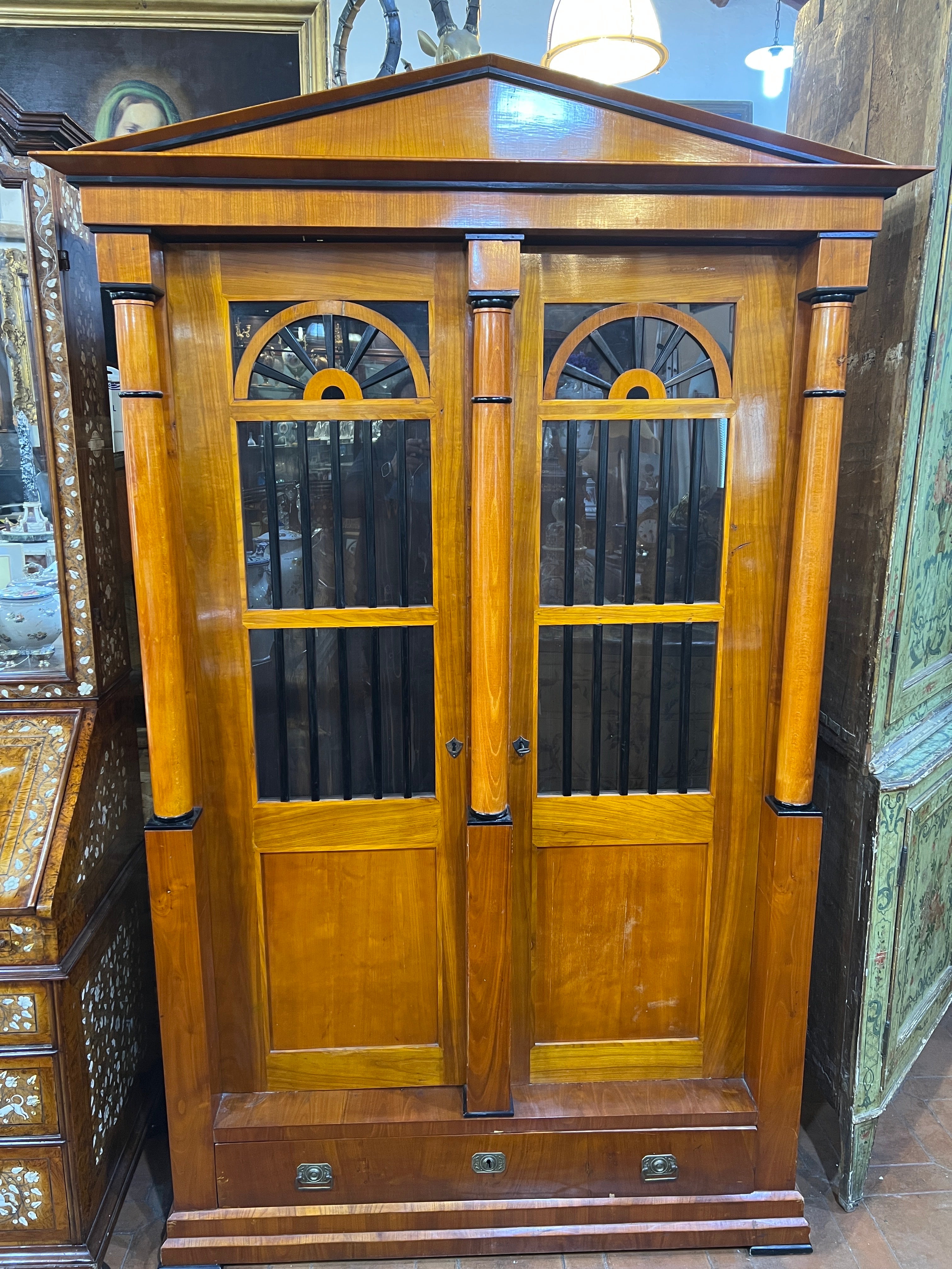 Fantastic two-door Vitrines cabinet of Austrian origin, early Biedermeier period ( 1815-1830), architectural form with a gable cap, giving the idea of the entrance to a Greek temple. Made of fir wood and plated with cherry wood, ebonized parts on