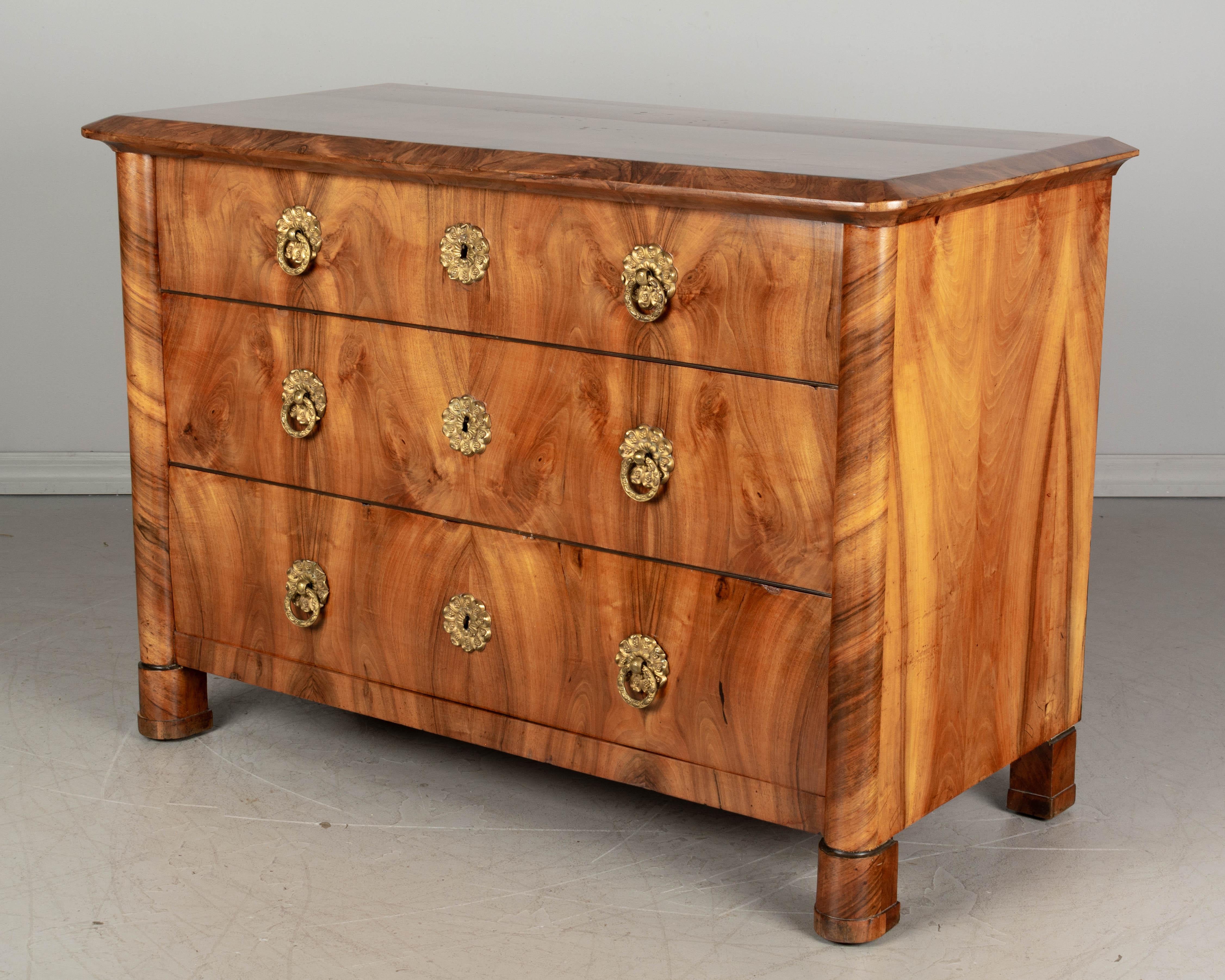 A fine 19th century Biedermeier commode from Austria made of book matched veneers of walnut over pine. Three dovetailed drawers with leaf form brass escutcheons and ring pulls. Beautiful choice of wood with swirling pattern on the front columns and