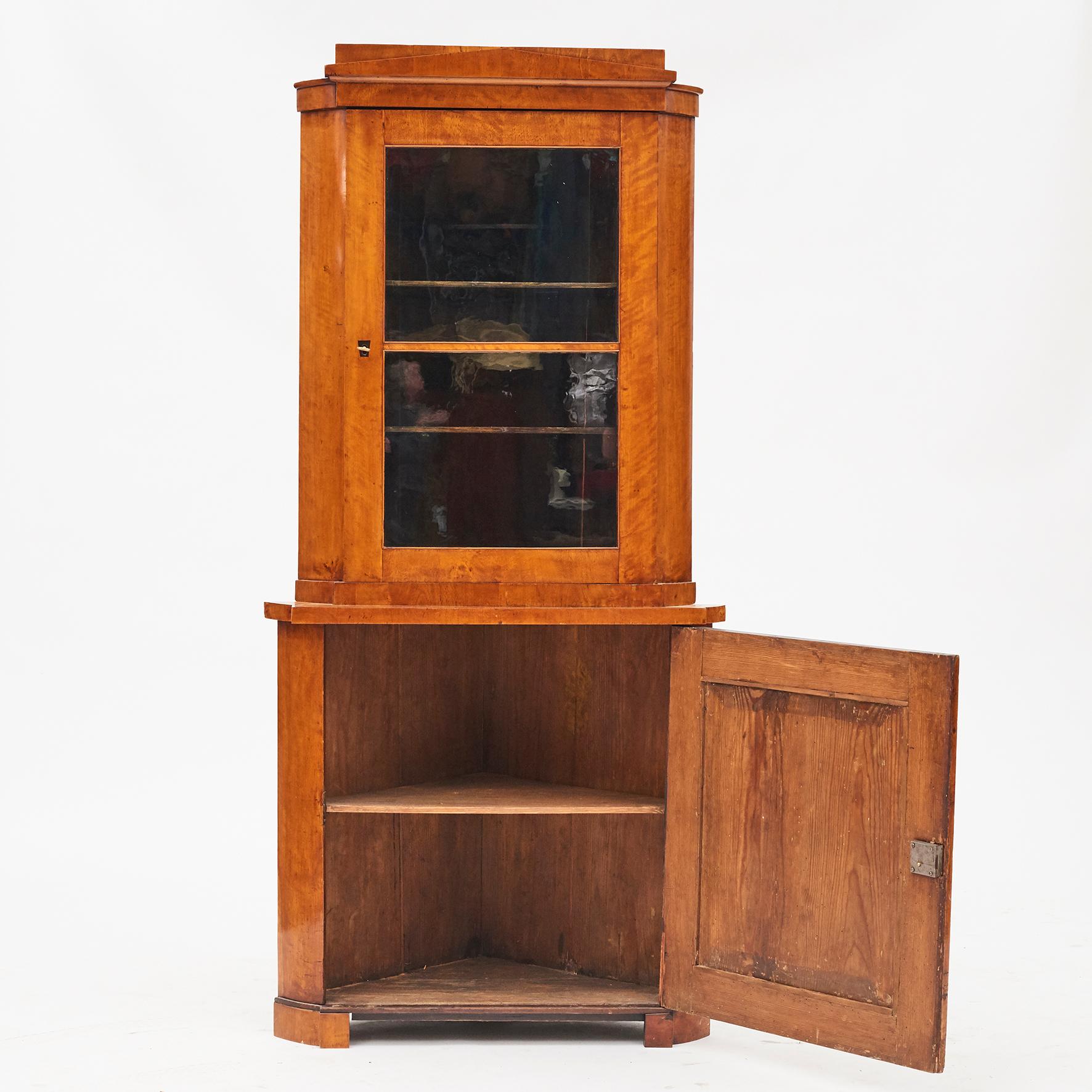 Biedermeier corner cabinet. Vienna, Austria, circa 1820-1830.

Pine veneered with flamed birch wood, beautiful grain and glow. Original condition with a light polished finish.
The cabinet is in two parts, upper part with 1 glass door, lower part