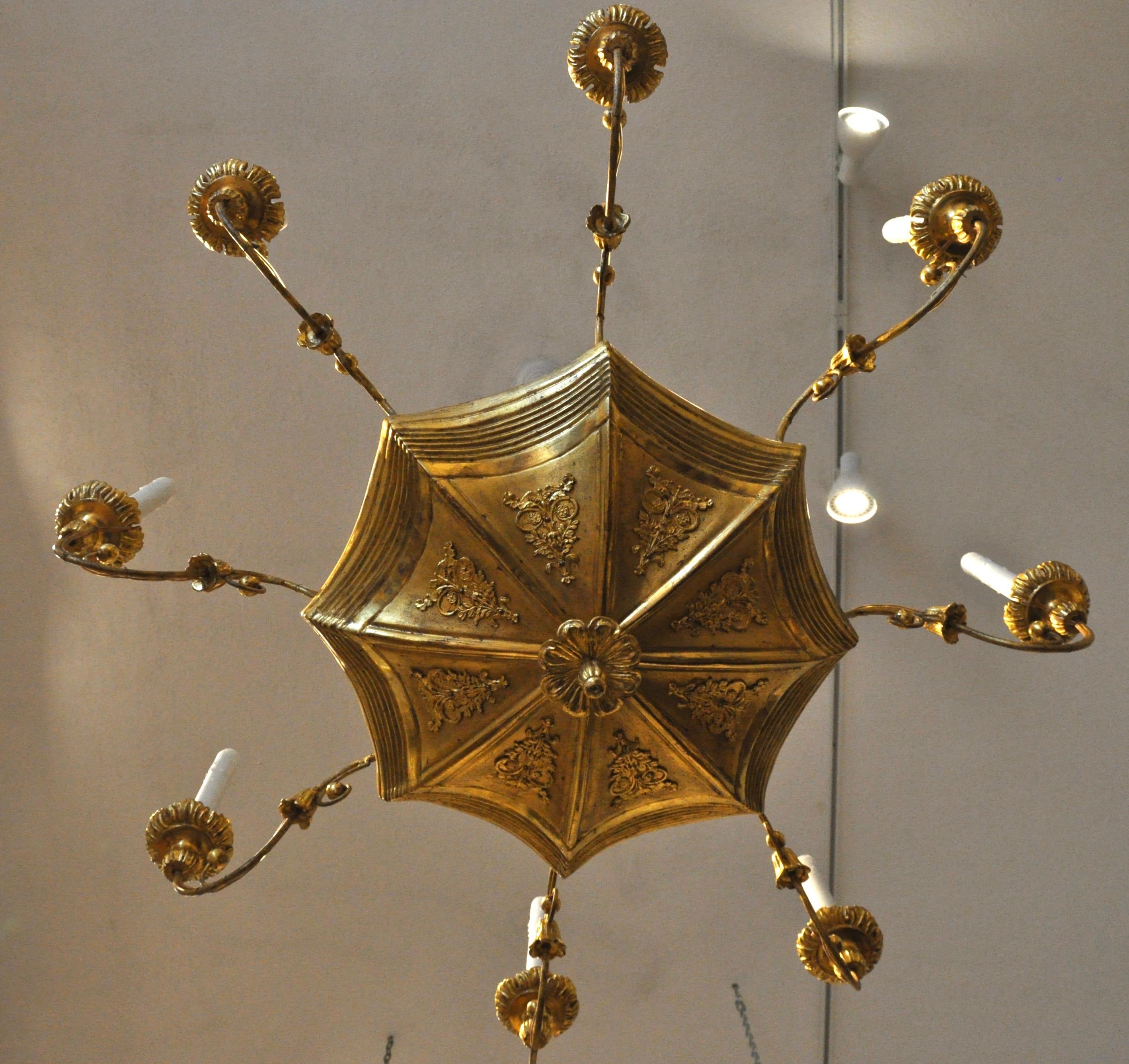 19th century giltwood neoclassical chandelier with eight arms

Carved and giltwood with iron arms of typical Empire form. Gilt applied metal mounts to bottom of umbrella. Now French wired. 
 