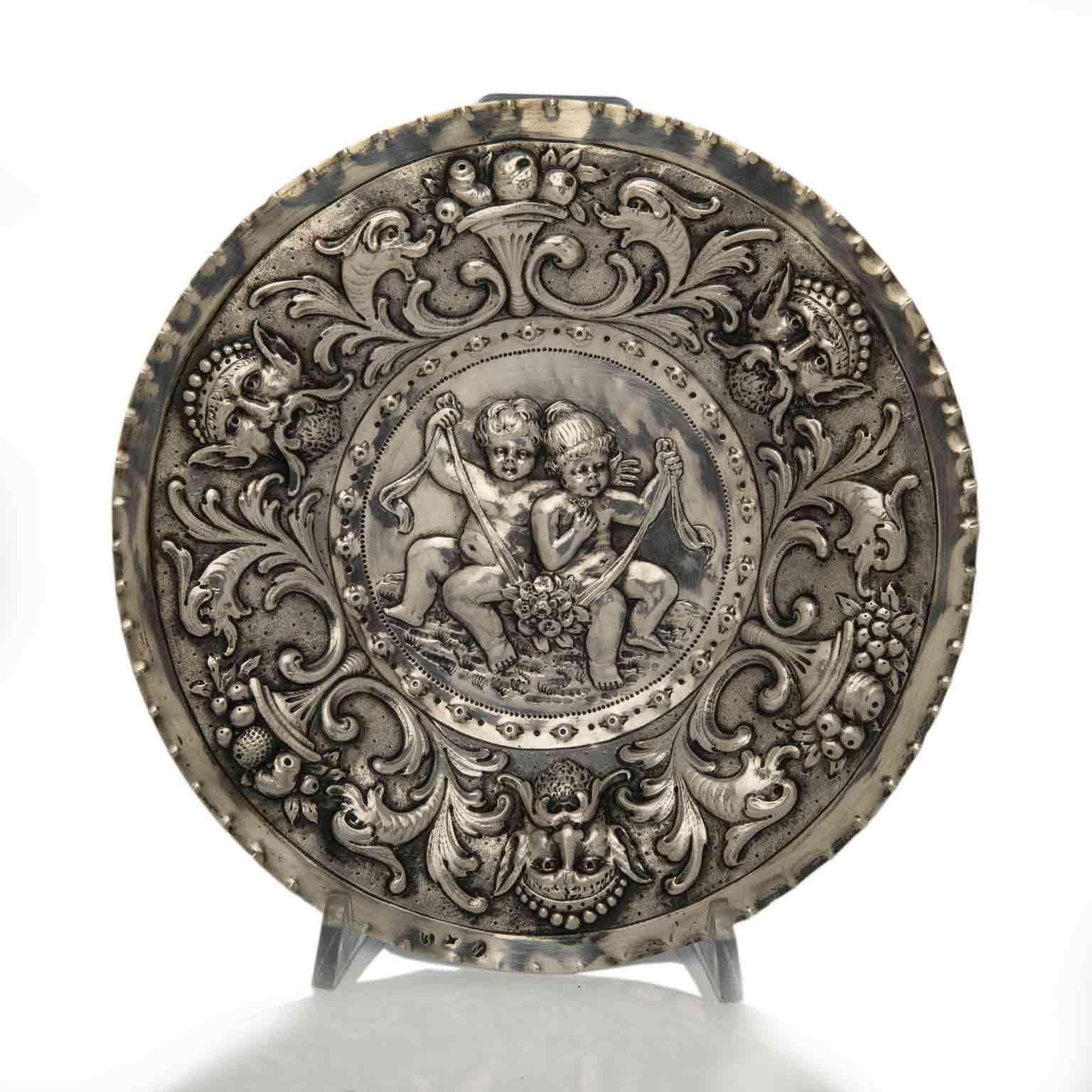 Lovely antique circular decorative silver dish, a round thick metal sheet centered by hand repoussé children figures playing with ribbons and flowers and superlative bas relief hand chased allegorical grottesques, scrolls and flowers on the round