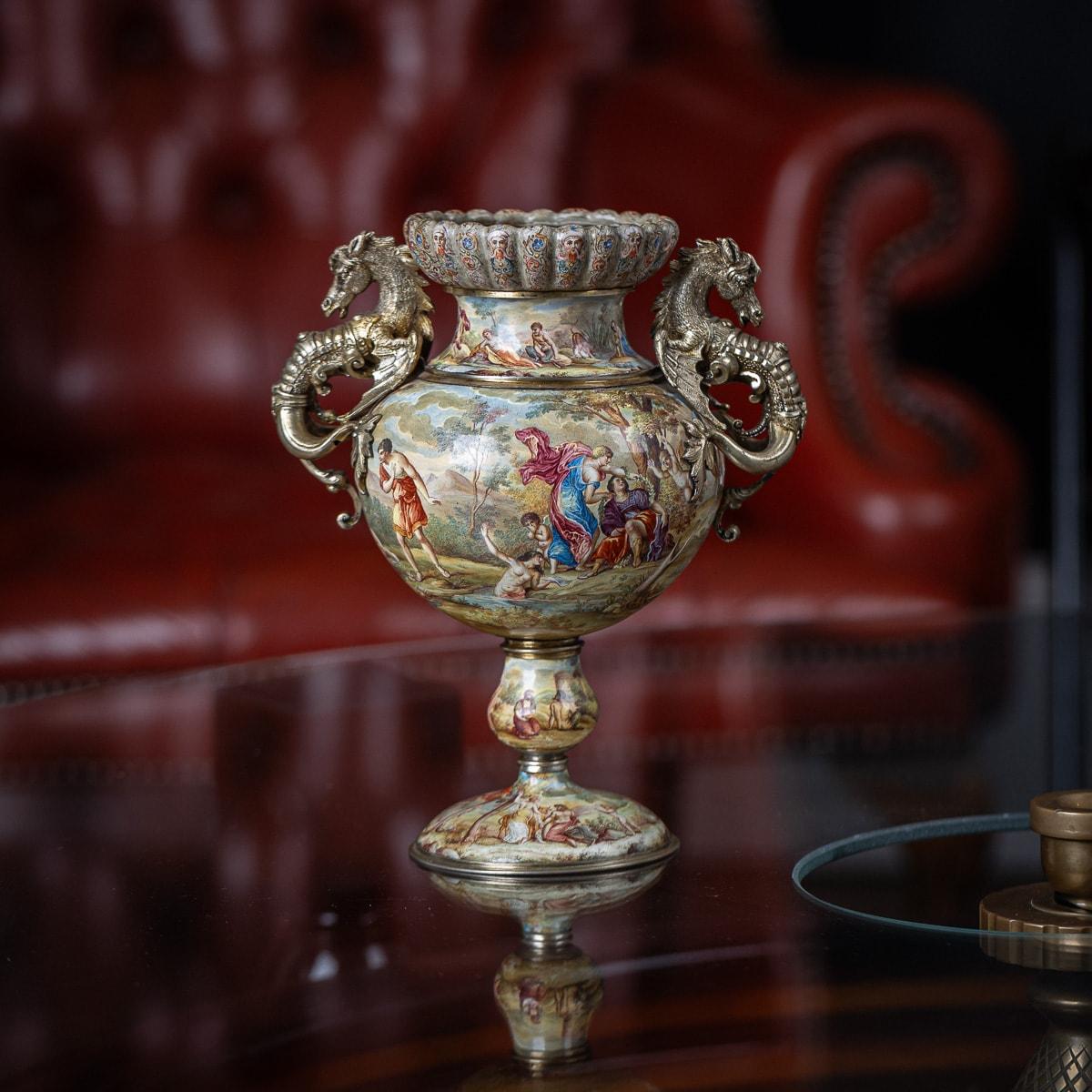 Antique late-19th Century Austrian exceptional solid silver gilt & enamel twin handled vase. Perched atop an oval base, its bulbous stem gracefully rises, while the body boasts intricate hand-painted classical allegorical scenes. Adorning its sides