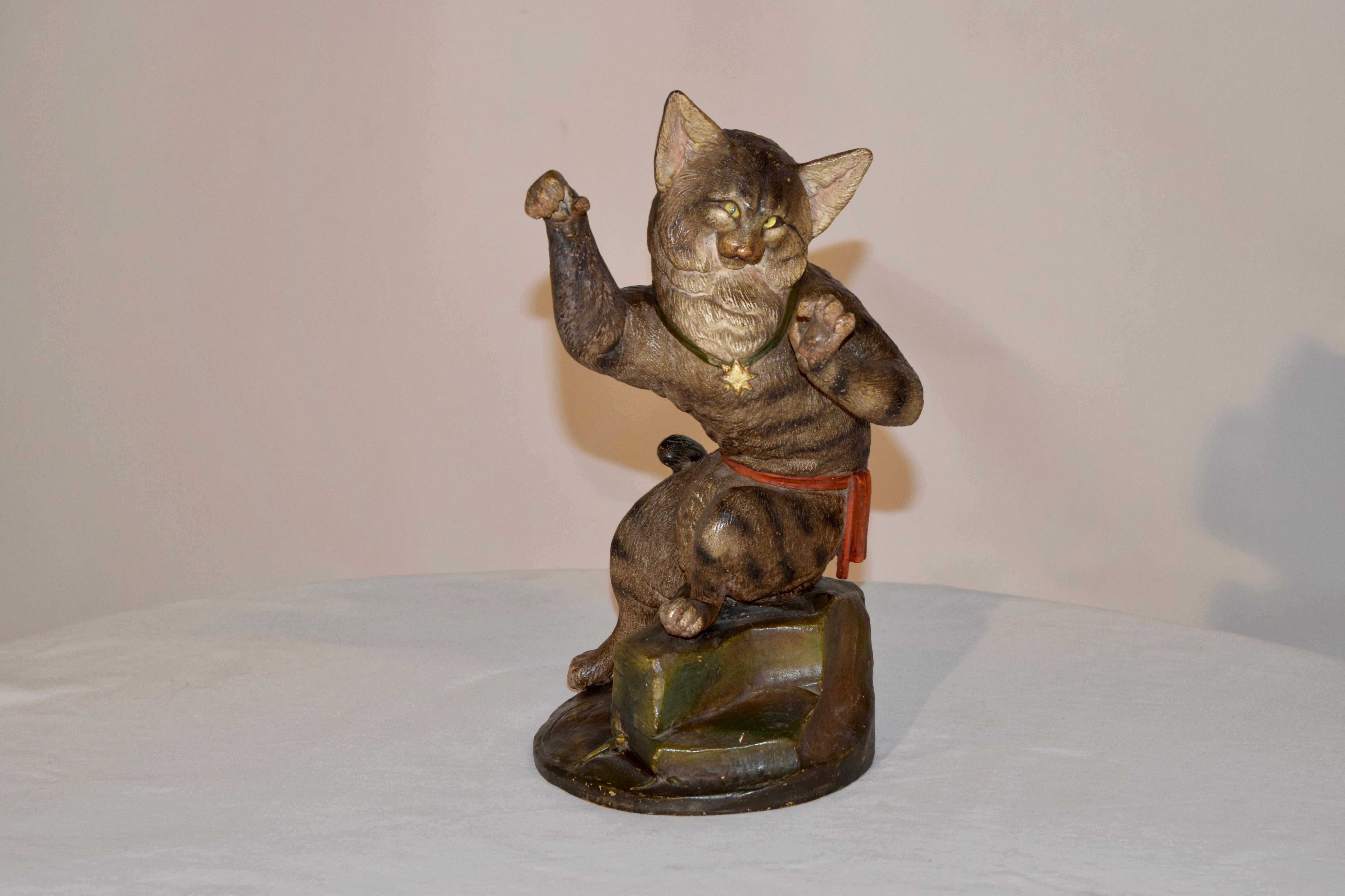 19th century Austrian terracotta cat figure with hand polychromed finish and glass eyes. The cat has a striped coat and is perched on a rocky surface with a red sash around his waist and a gold star medal on a green ribbon around his neck. Very