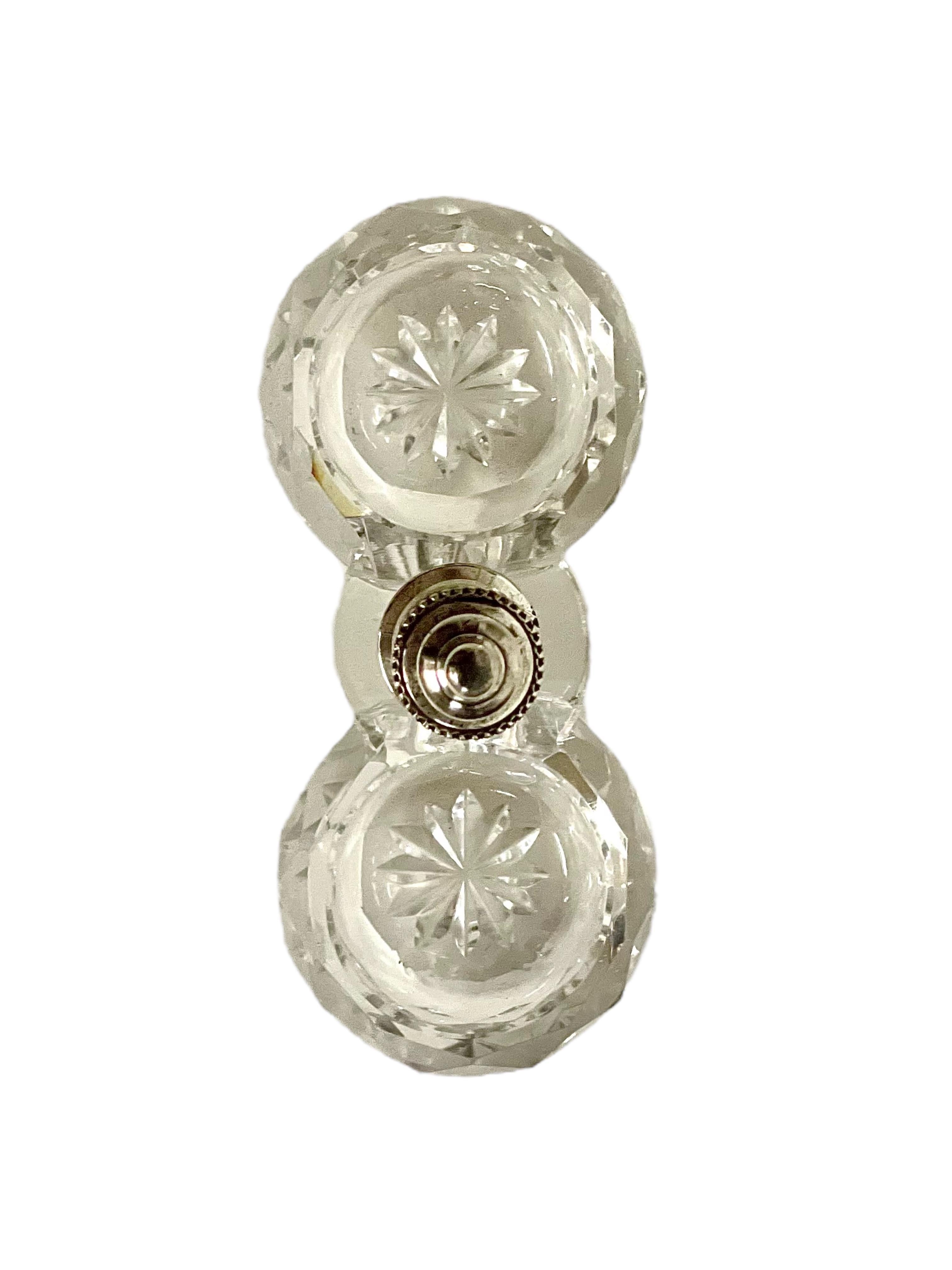 Cette double salière ouverte scintillante, fabriquée par le célèbre cristallier Baccarat, est faite d'une pièce de verre solide et d'un élégant bouton argenté surmonté d'un fleuron qui sépare les deux coupes. Chaque assiette creuse est ornée de