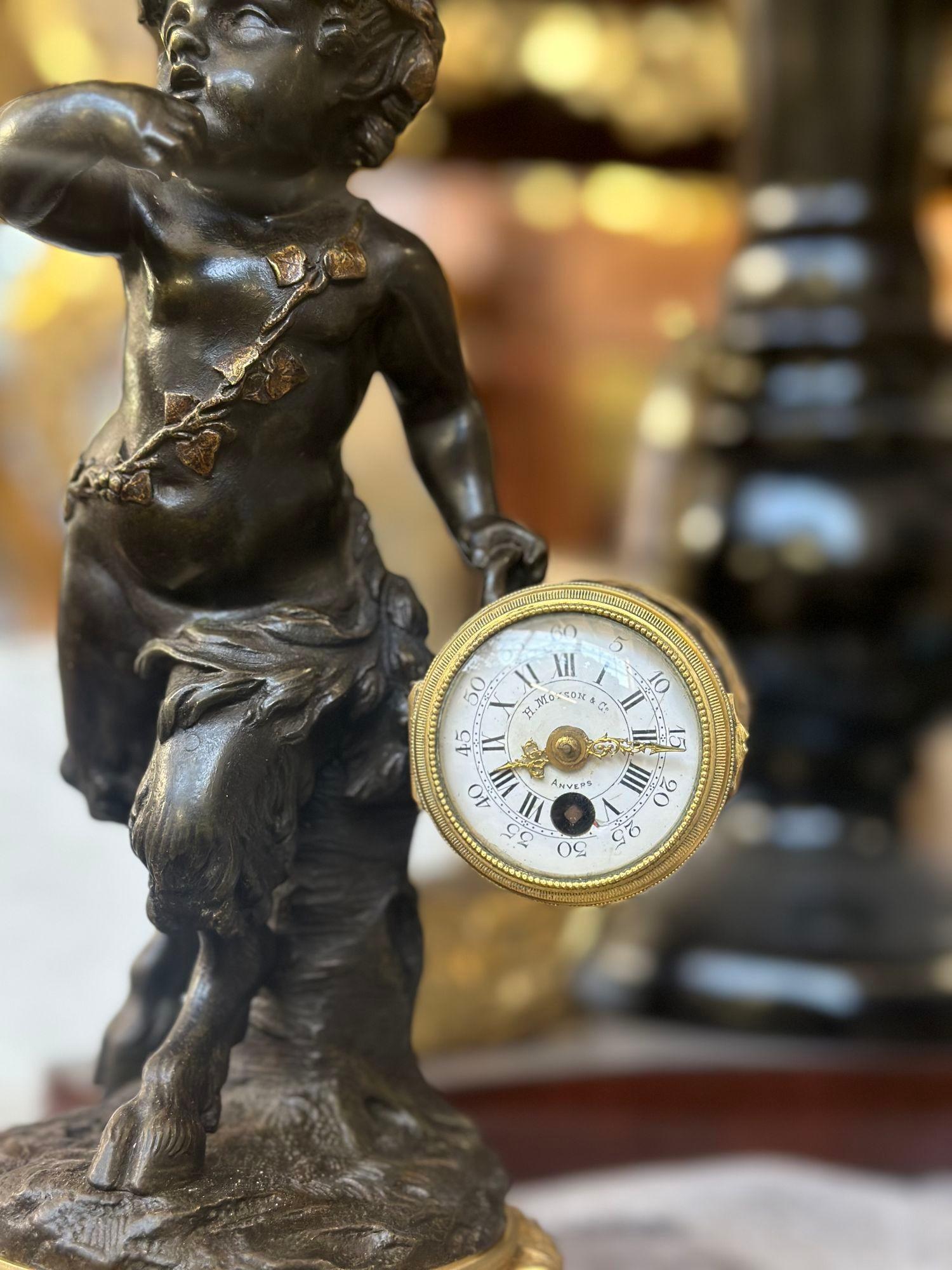 Gorgeous and mythical sculptural clock made of patinated and gilt bronze, depicting a young Bacchanalian faun wearing a leaf crown on his head and a grape leaf sash around his body. He is holding a drum-form clock which is marked 