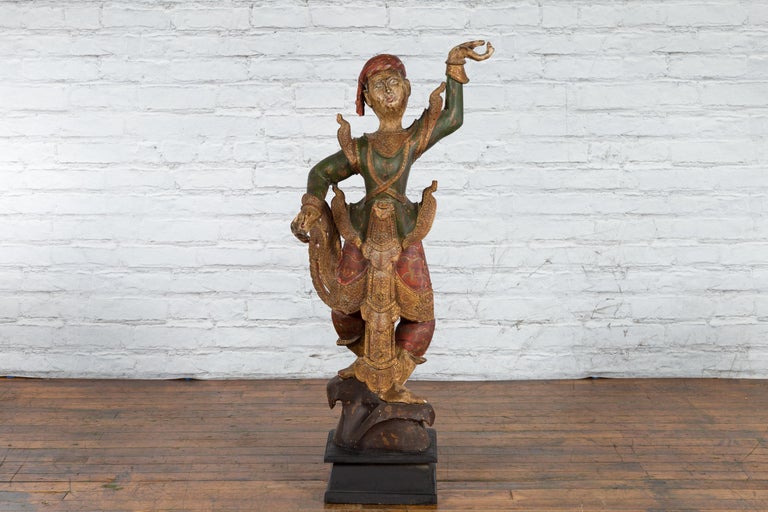 A tall antique Balinese hand-carved and painted wooden statue from the 19th century on black base. Hand-made on the island of Bali, Southern Indonesia during the 19th century, this wooden sculpture captures our attention with its lively attitude and