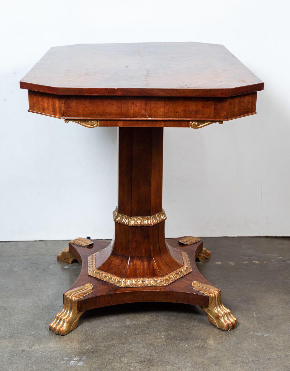 Hand-carved, parcel-gilt, mahogany, single drawer, writing table. The clipped corner, inlaid top rests on an octagonal pedestal and the whole sits on a convex base finished with gilded, paw feet.