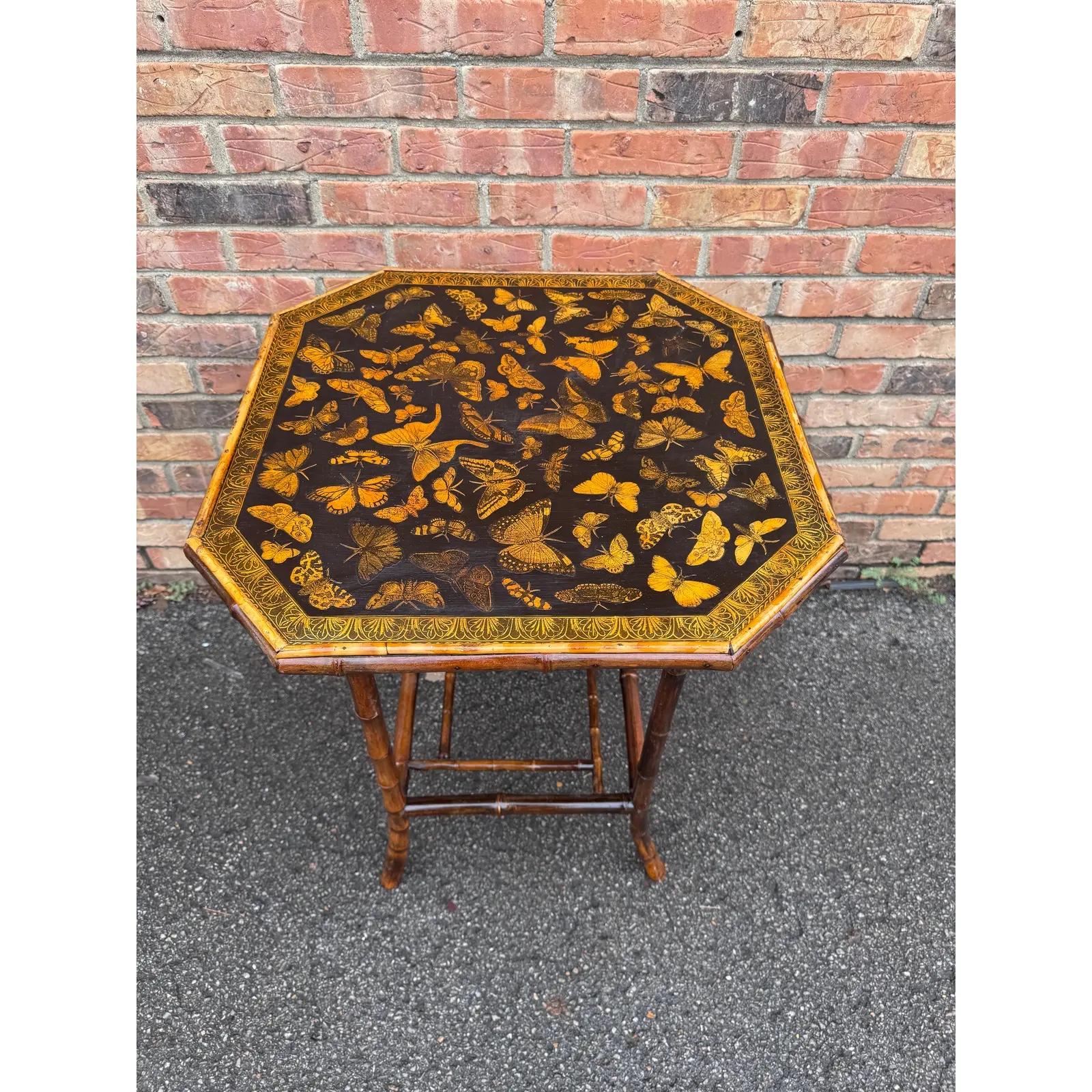 Esta mesa auxiliar inglesa de bambú del siglo XIX con decoupage presenta una deliciosa variedad de mariposas y flores decoupageadas en la parte superior y en el estante decorativo inferior. Sería una bonita mesilla de noche, junto a una silla, una