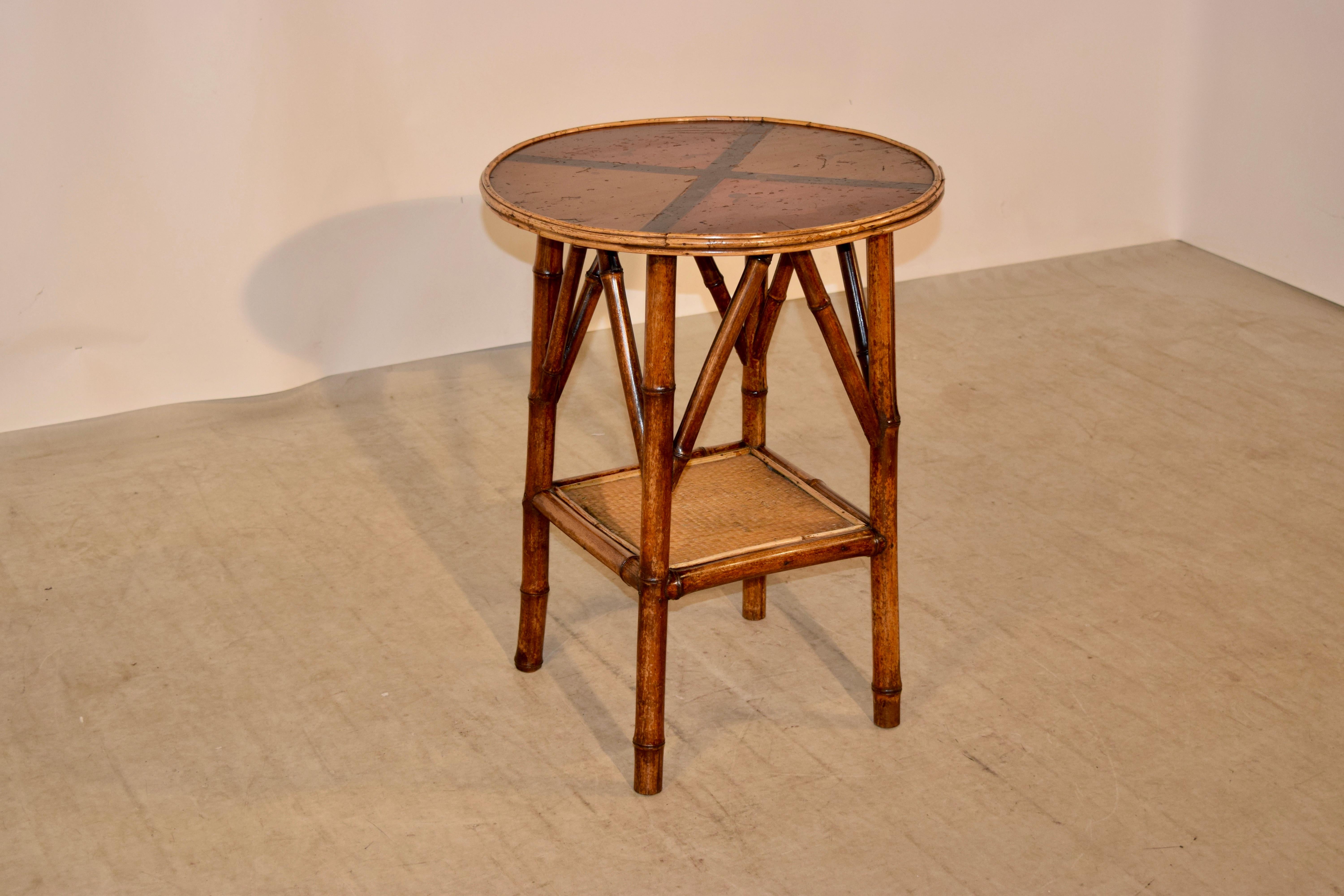19th century bamboo side table from France with a round top with a hand painted top and bamboo banding around the edge, following down to bamboo legs joined by a lower shelf, which is covered in rush.
