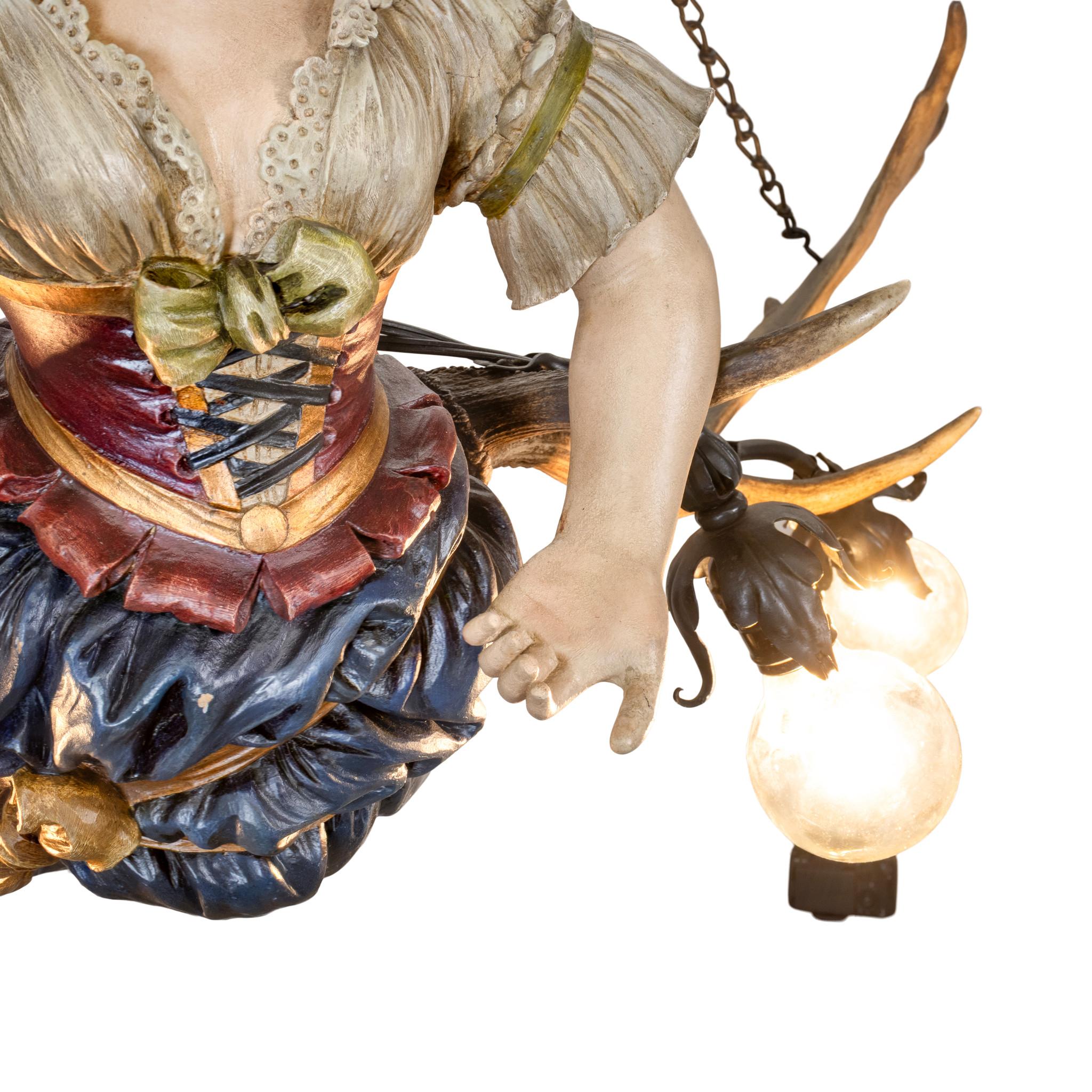 Lampadario a sospensione in corno e fanciulla da bar del XIX secolo. Realizzato con corna di daino. Figura di cameriera da bar squisitamente scolpita con corsetto rosso allacciato e gonna blu. Ben dipinto con colori vivaci. Appeso in un pub tedesco.