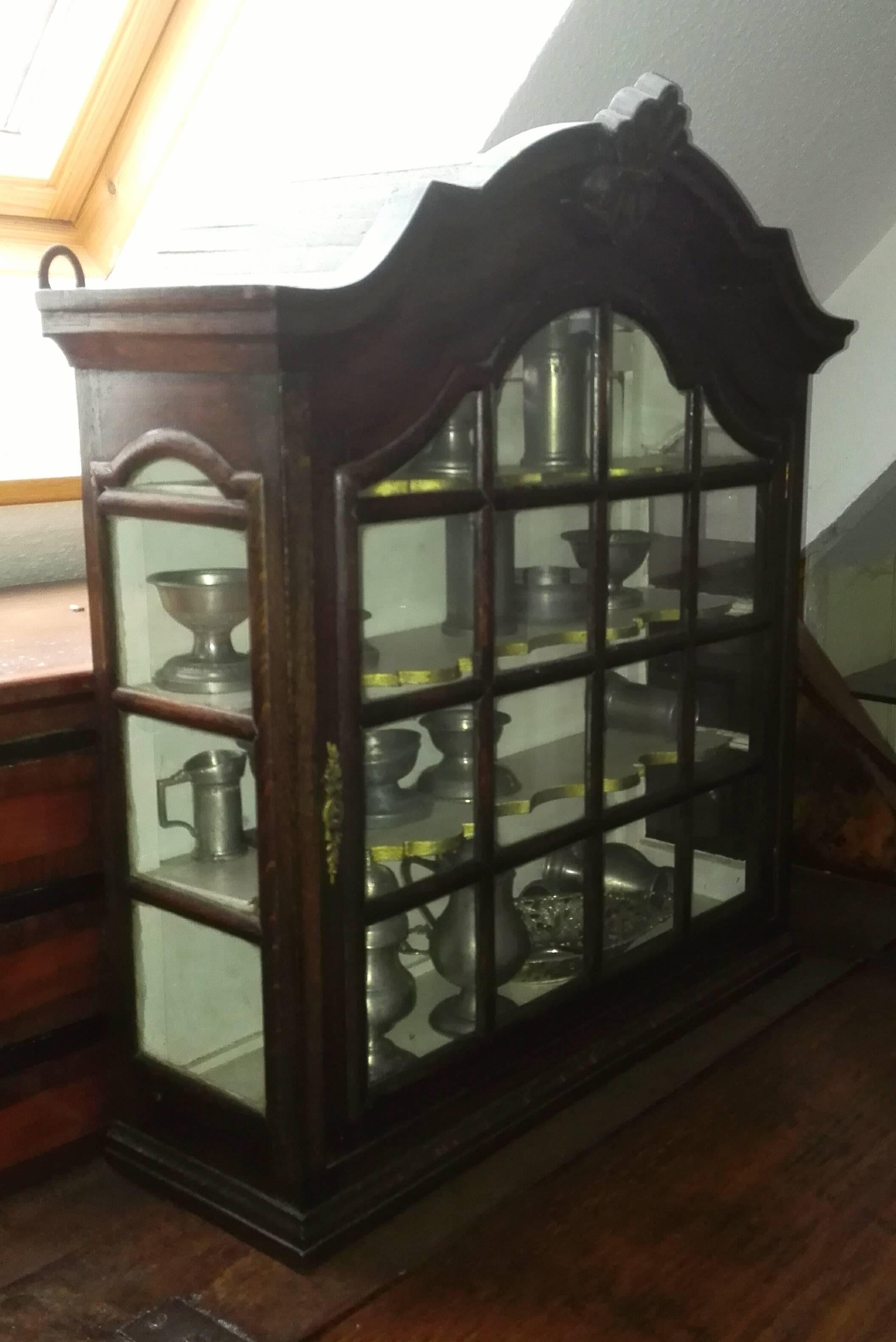 This small , but very well-proportioned hanging display case (known in Germany as Buddelei), dates from the second half of the 19th century and is made of solid black - brown patinated oak!
The double-curved head shape with capstone (cartouche),