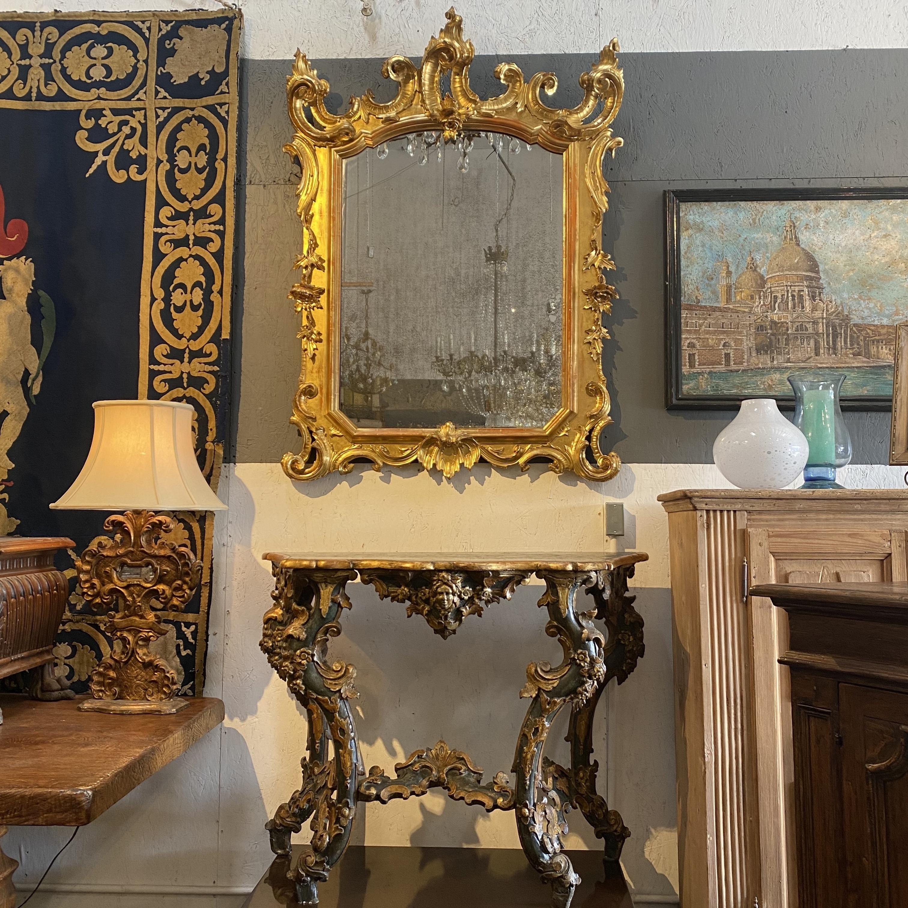Spectaculaire cadre de miroir de style baroque italien, en bois magnifiquement sculpté et doré avec des volutes végétales, des fleurs et des feuilles, et des sommets couronnés. Un mélange glamour de détails grandioses et délicieux, qui ne manquera