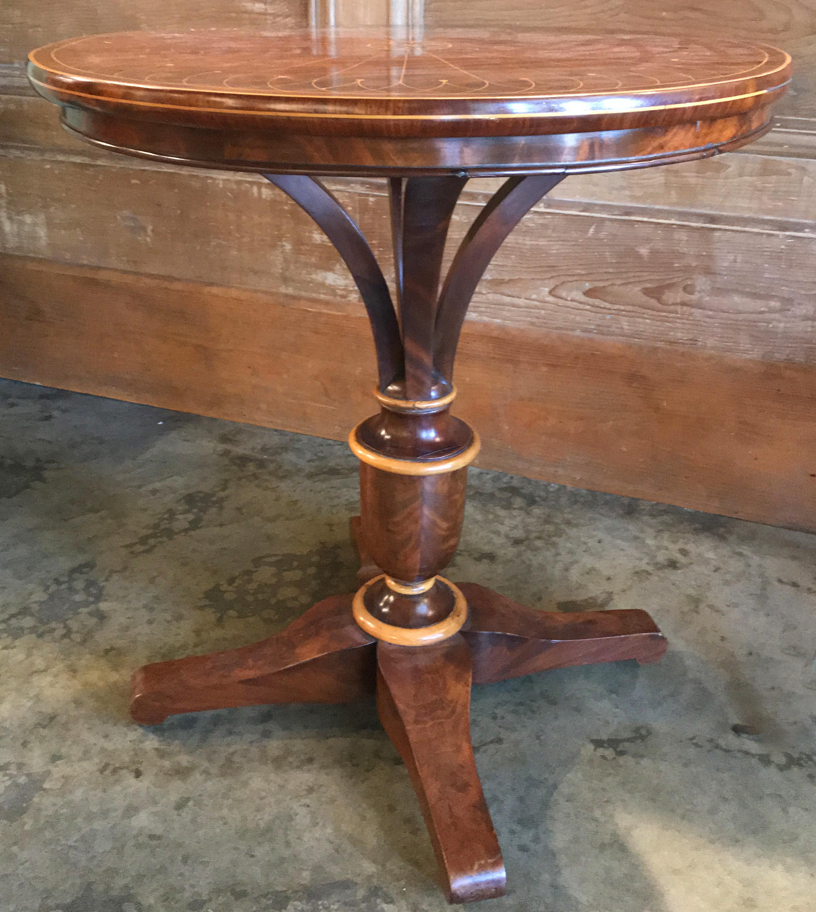 An exquisite Biedermeier round top mahogany center table with radiating line inlay, raised by an urn form pedestal with fruitwood highlights and four carved feet. Dates to the 19th century in very good condition, with repairs and restorations to the