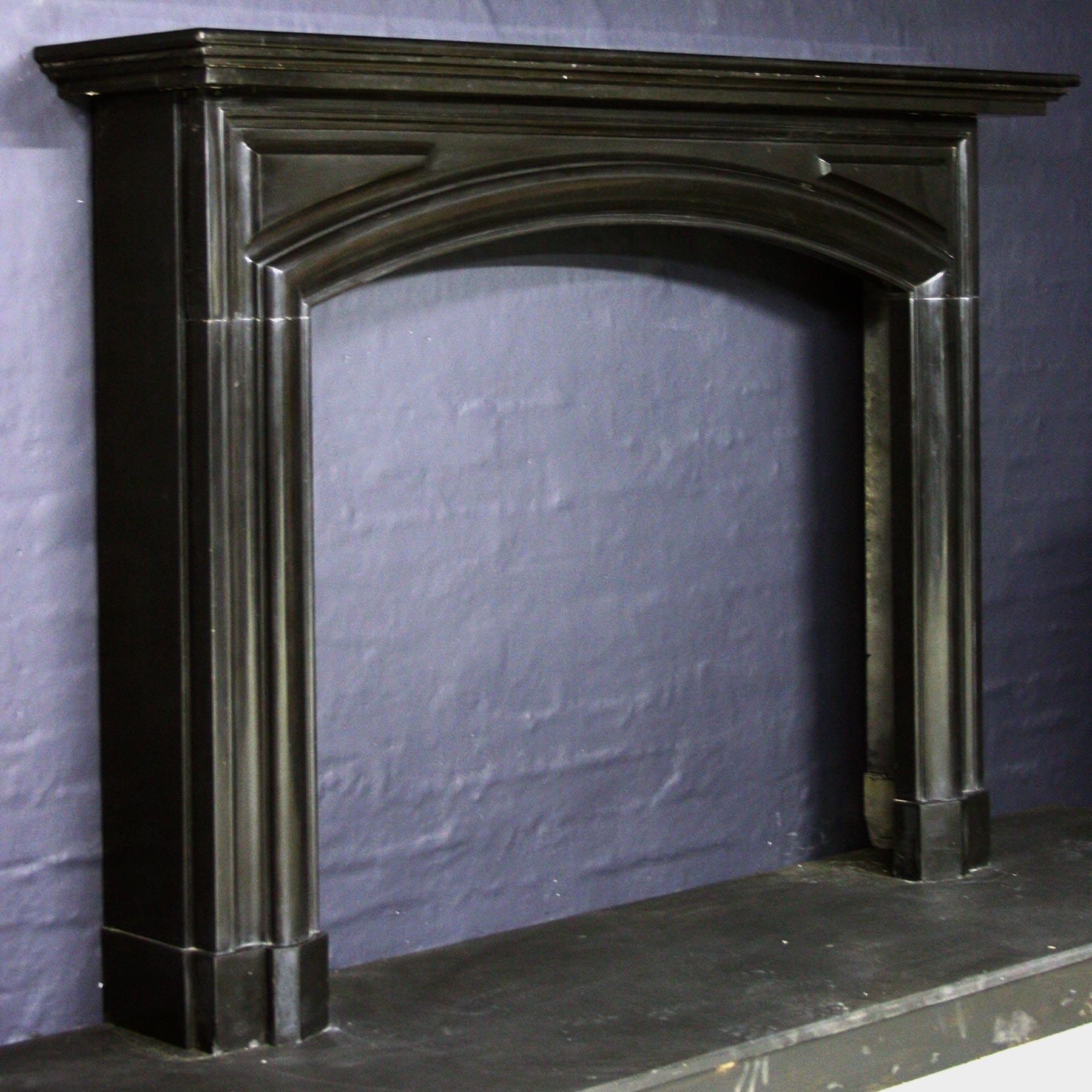 A 19th century Belgian black chimneypiece, with a moulded architectural shelf, arched frieze with raised and fielded panels, and a bold Bolection moulding continuing down the jambs - framing the aperture - all on block feet.