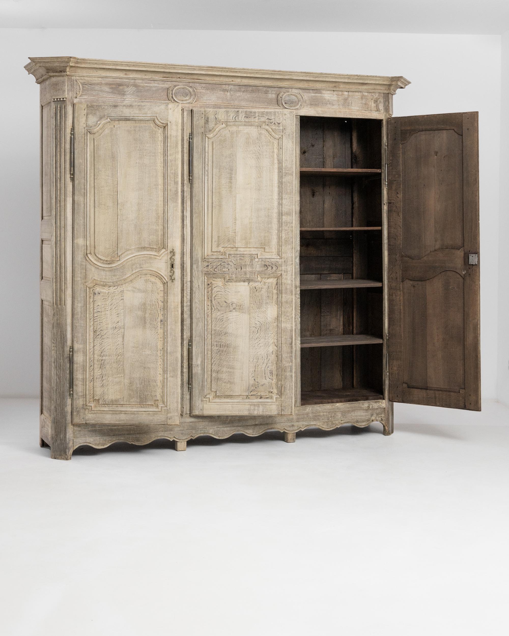 Cette armoire belge, fabriquée vers 1850, est dotée d'une noble finition en chêne pâle qui met en valeur sa présence majestueuse. Grand et ample, le coffre offre un espace pléthorique divisé en trois sections par des portes surélevées avec des