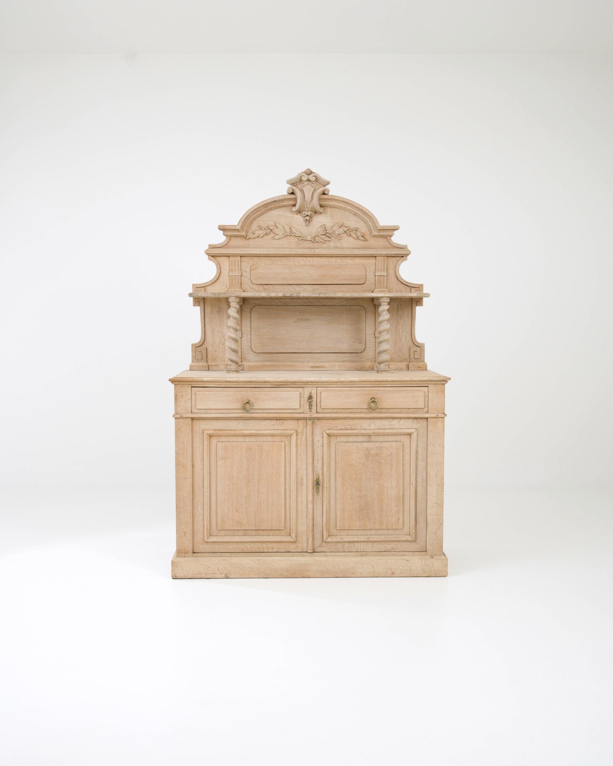 Handcrafted out of solid European oak in the 19th century, this Belgian cupboard offers a distinctive design with elaborate ornamental accents. Twisted columns support the upper display shelf, complemented by meticulous foliate carvings and an