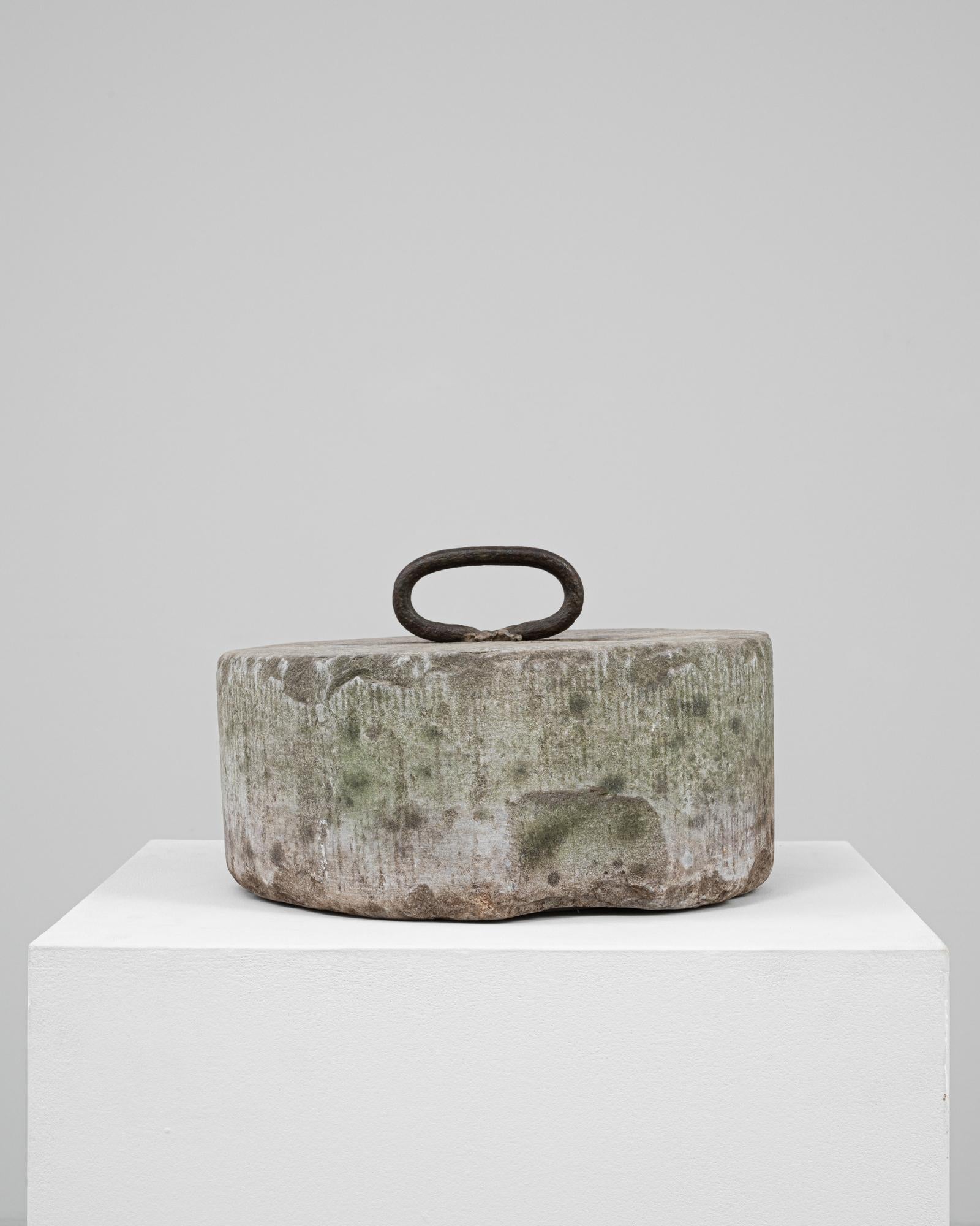 This 19th Century Belgian concrete door stop is a grounded, sculptural object that speaks to both function and form. Cast in a wide, low cylindrical shape, its surface is deeply weathered with subtle linear textures and a natural patina in earthy