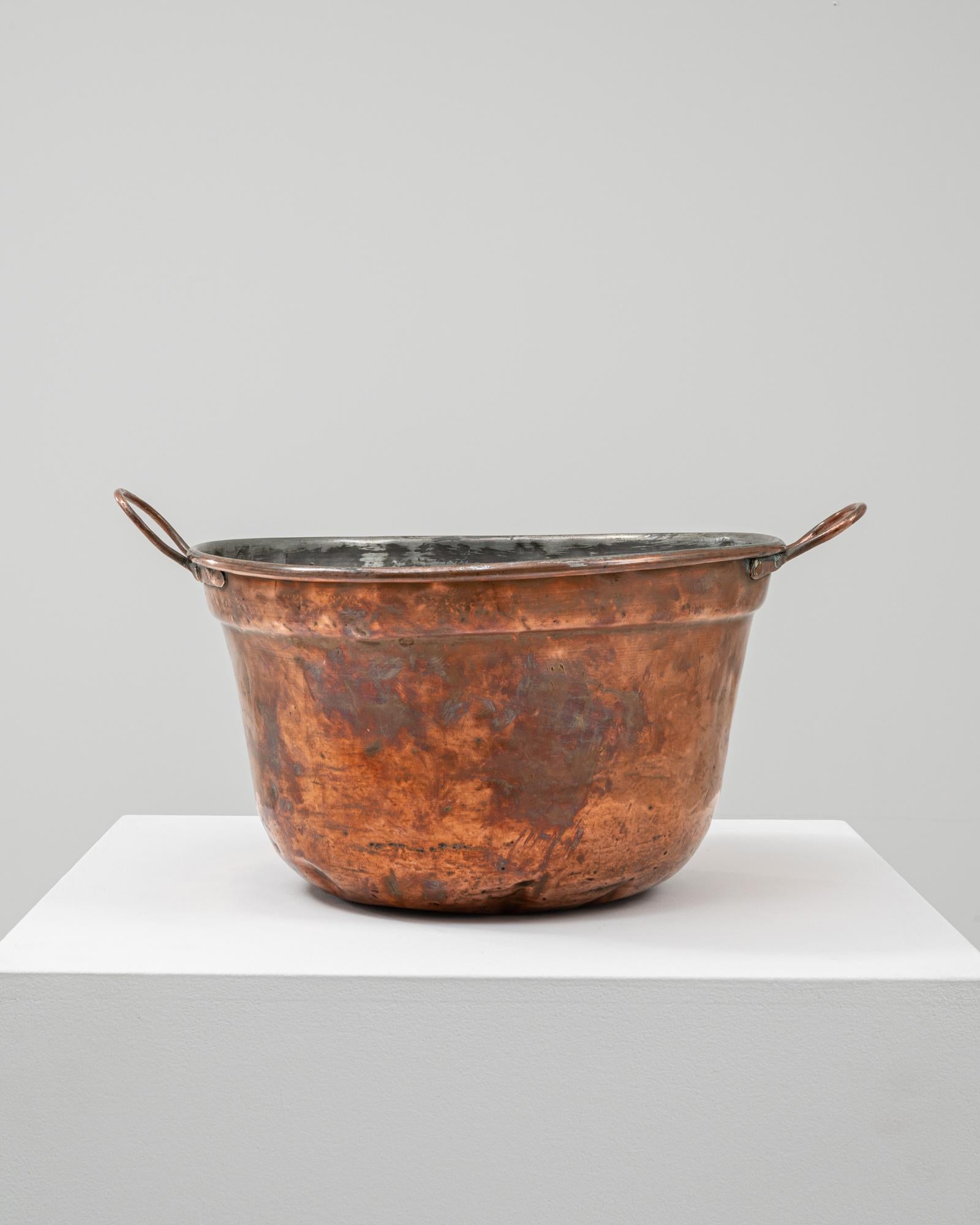 This 19th-century Belgian copper pot showcases expert craftsmanship and utilitarian elegance. Hand-hammered from solid copper, it features a deep basin with a gently flared rim and rounded base, ideal for cooking or heating liquids in traditional