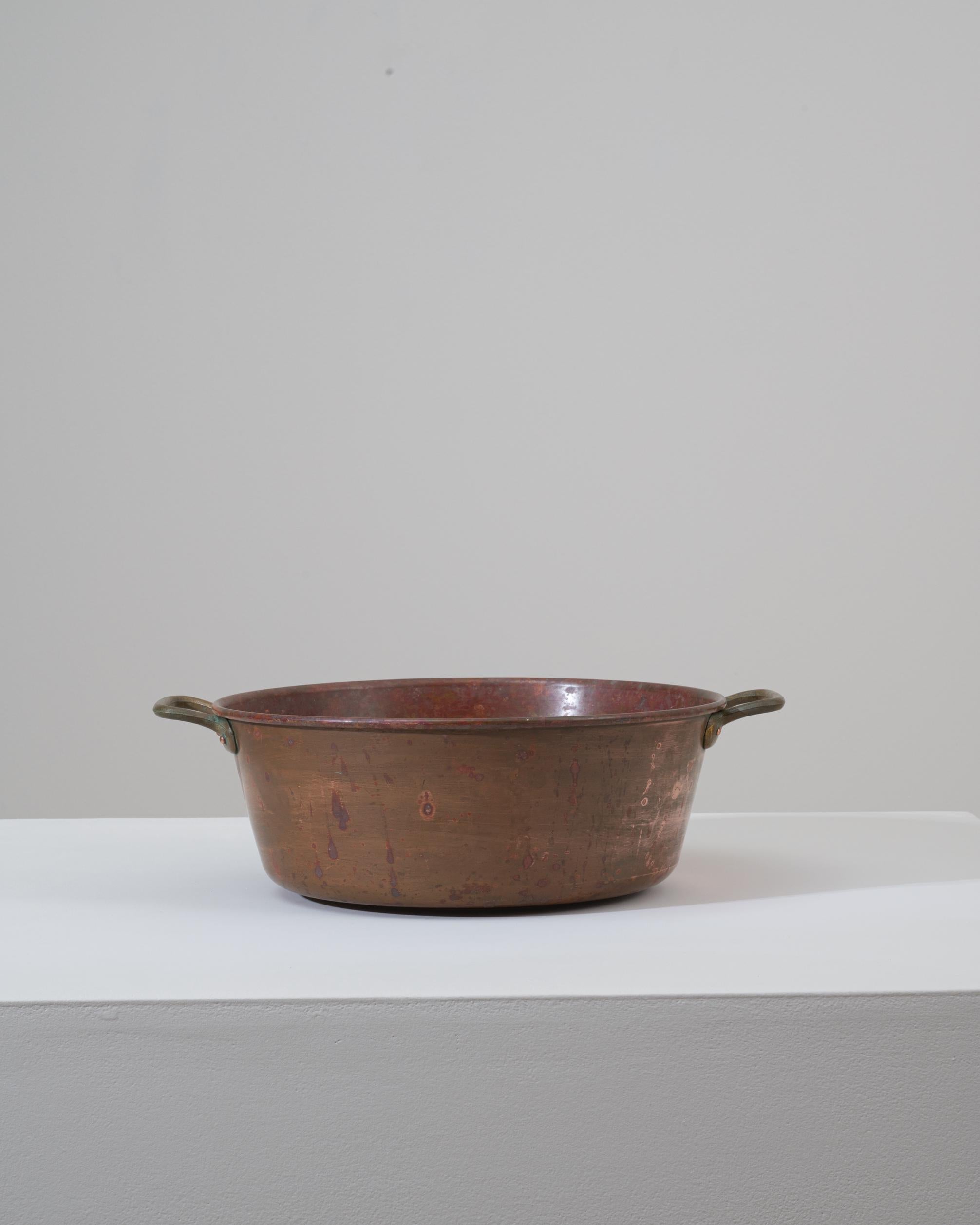 Questa pentola in rame belga del XIX secolo presenta un carattere caldo e vissuto che riflette le sue origini utilitarie e la sua duratura abilità artigianale. Formata a mano con un corpo ampio e delicatamente svasato, presenta una patina ricca e
