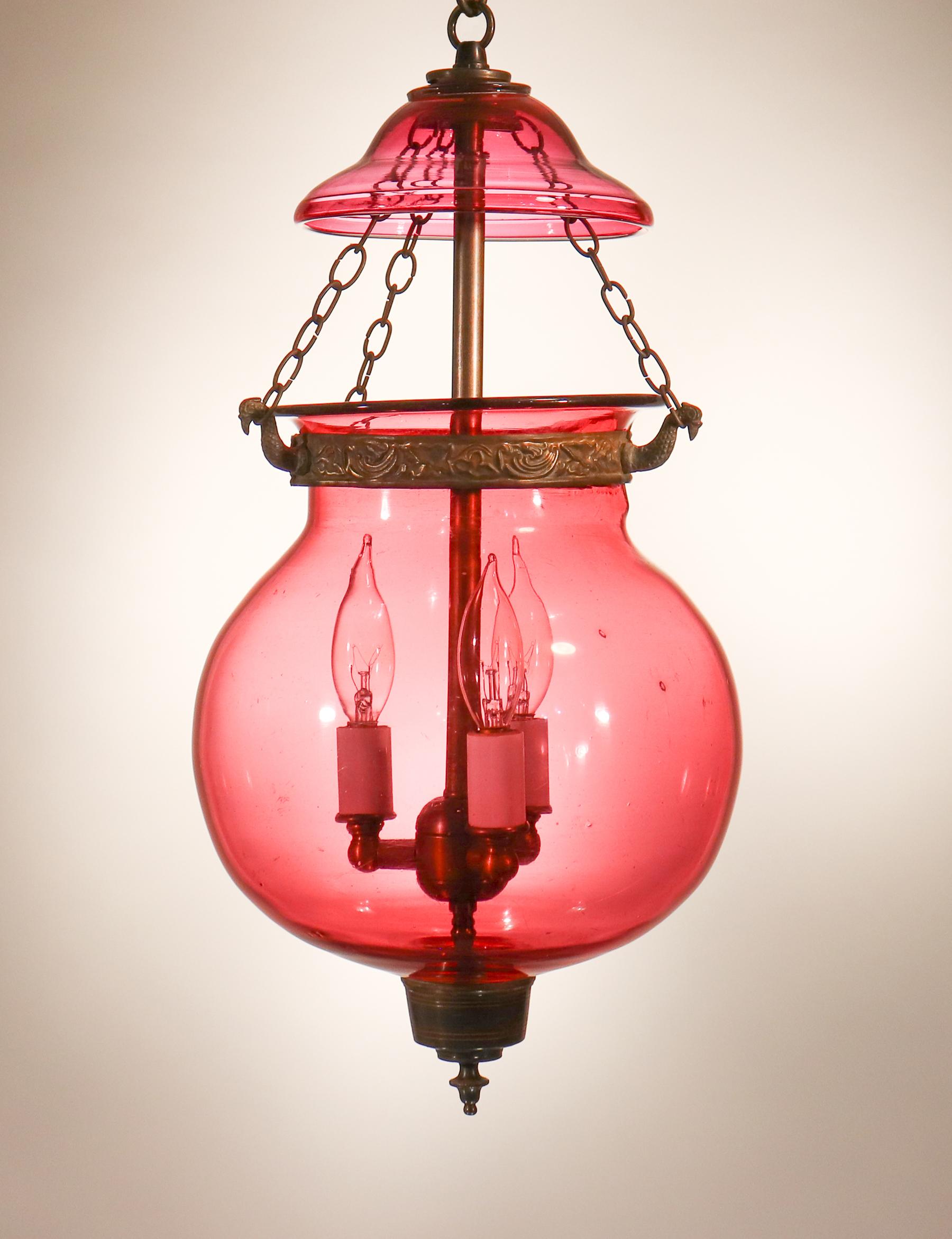 A charming and rare cranberry-colored hand blown glass globe bell jar lantern from Belgium, circa 1890, with attractive form and its original embossed brass band and chains. The globe's collar has the manufacturer's pressed mark, 