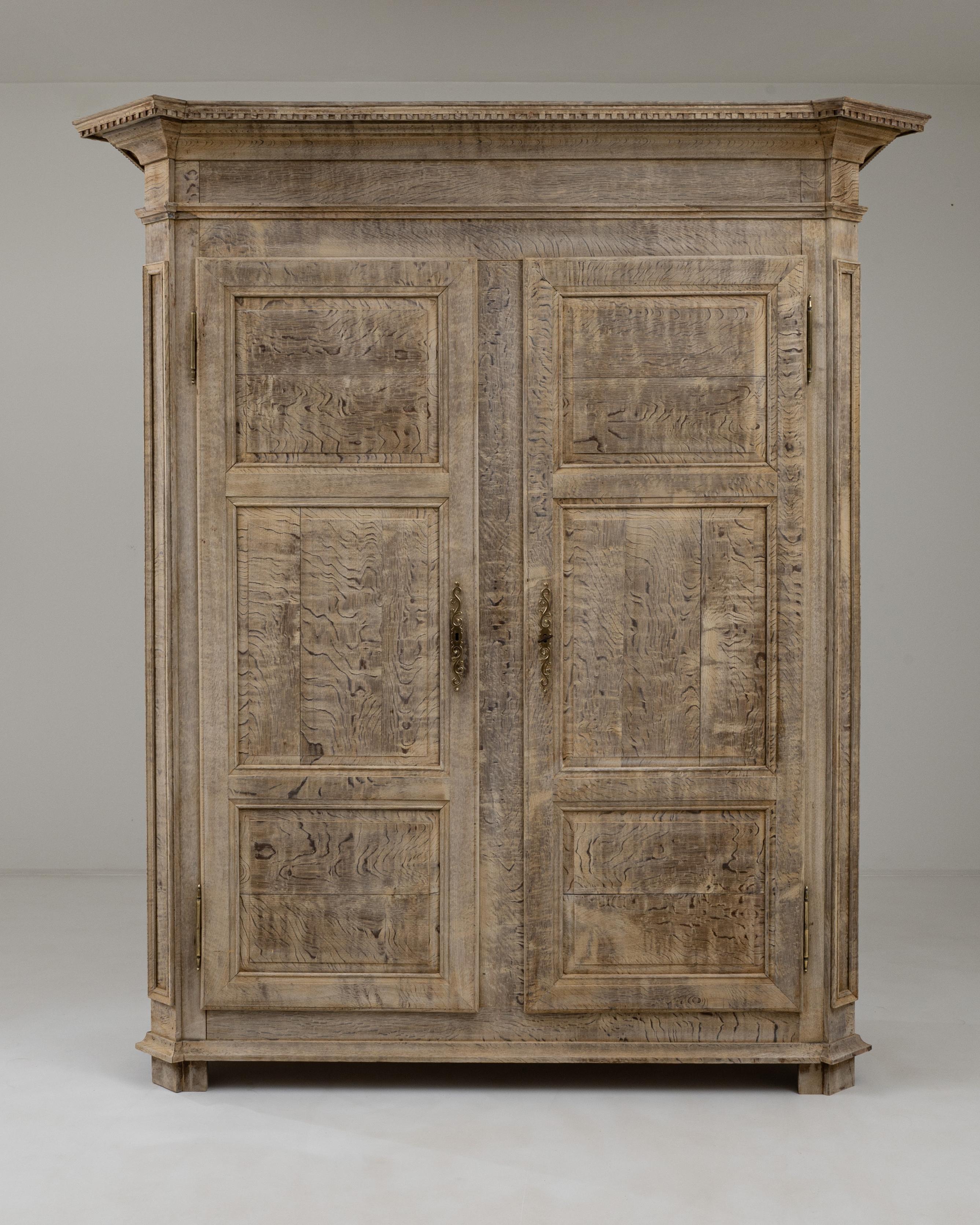 The commanding presence of this 19th-century Belgian cabinet is accentuated by its gracefully molded cornice, adorned with carved decorative elements along its edges. The panel doors and beveled corners contribute to its balanced symmetry, revealing