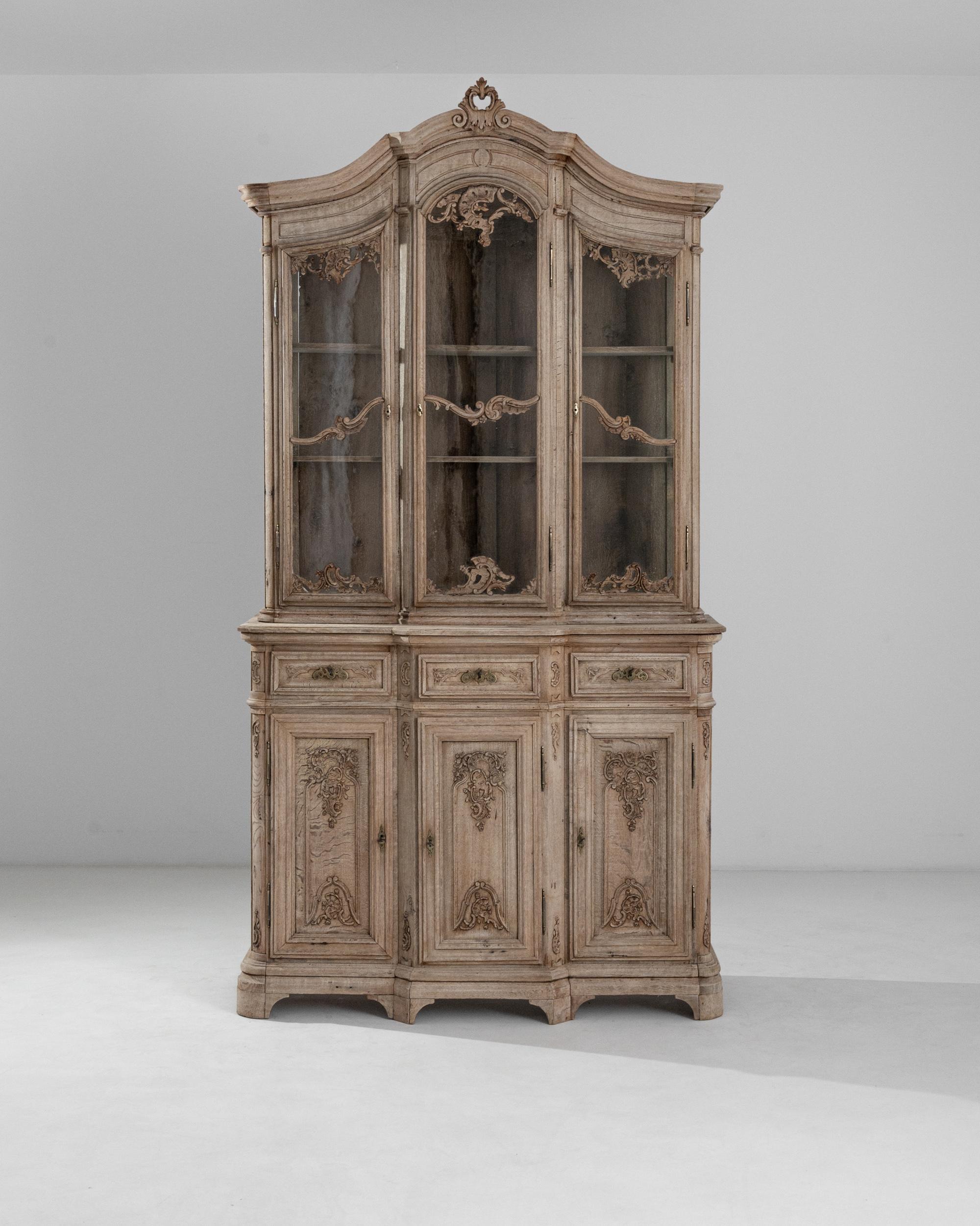 The exquisite carved accents which adorn this antique rococo vitrine create an impression of effervescent spontaneity. Built in Belgium in the 19th century, the piece is distinguished by the flourishes of leaves and flowers which appear to overflow