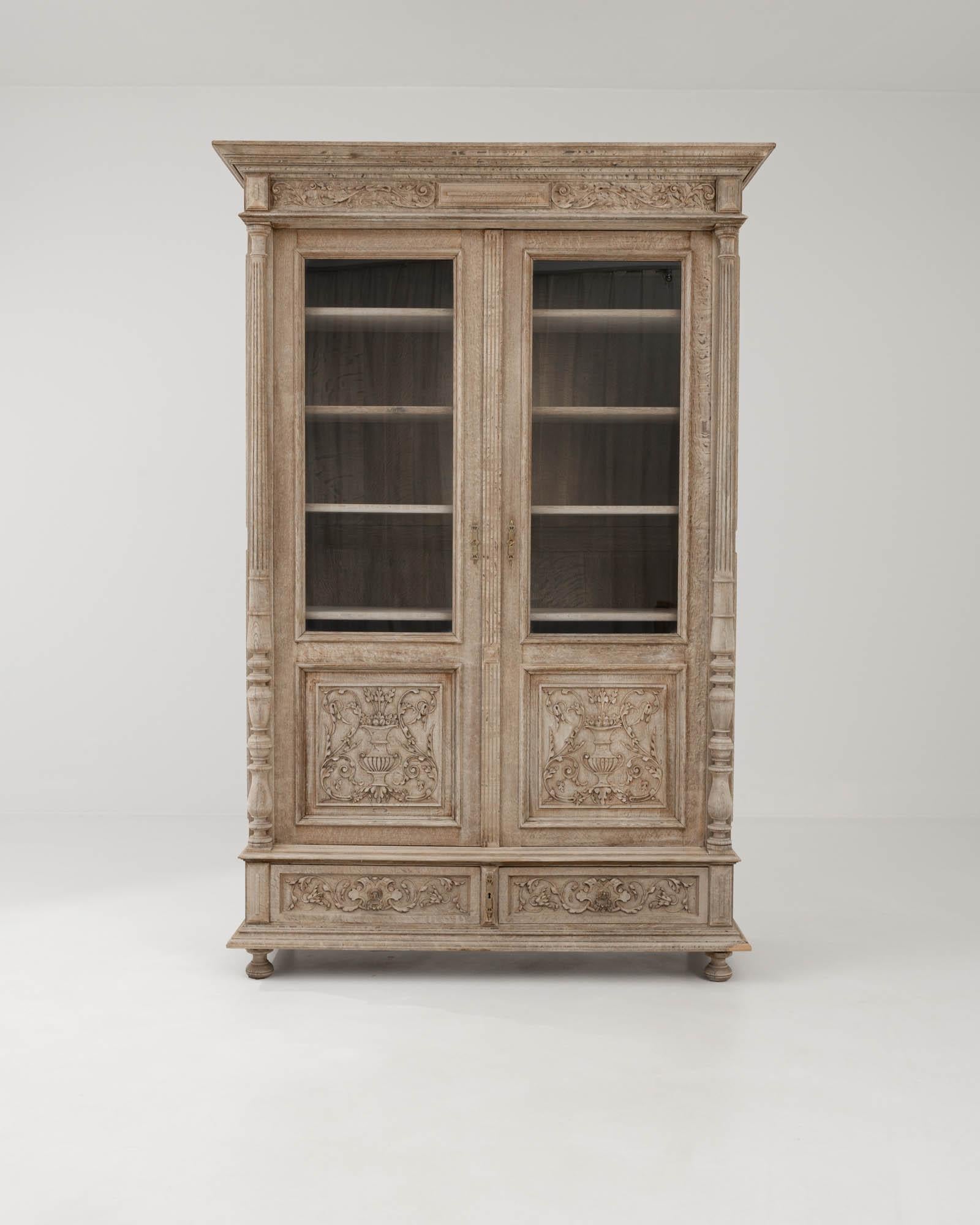 Combining the clean symmetries of Neoclassical style with the verdant excesses of the Rococo aesthetic, this ornate oak vitrine offers a majestic antique centerpiece. Hand-crafted in Belgium in the 1800s, the panels of the cabinet are carved with