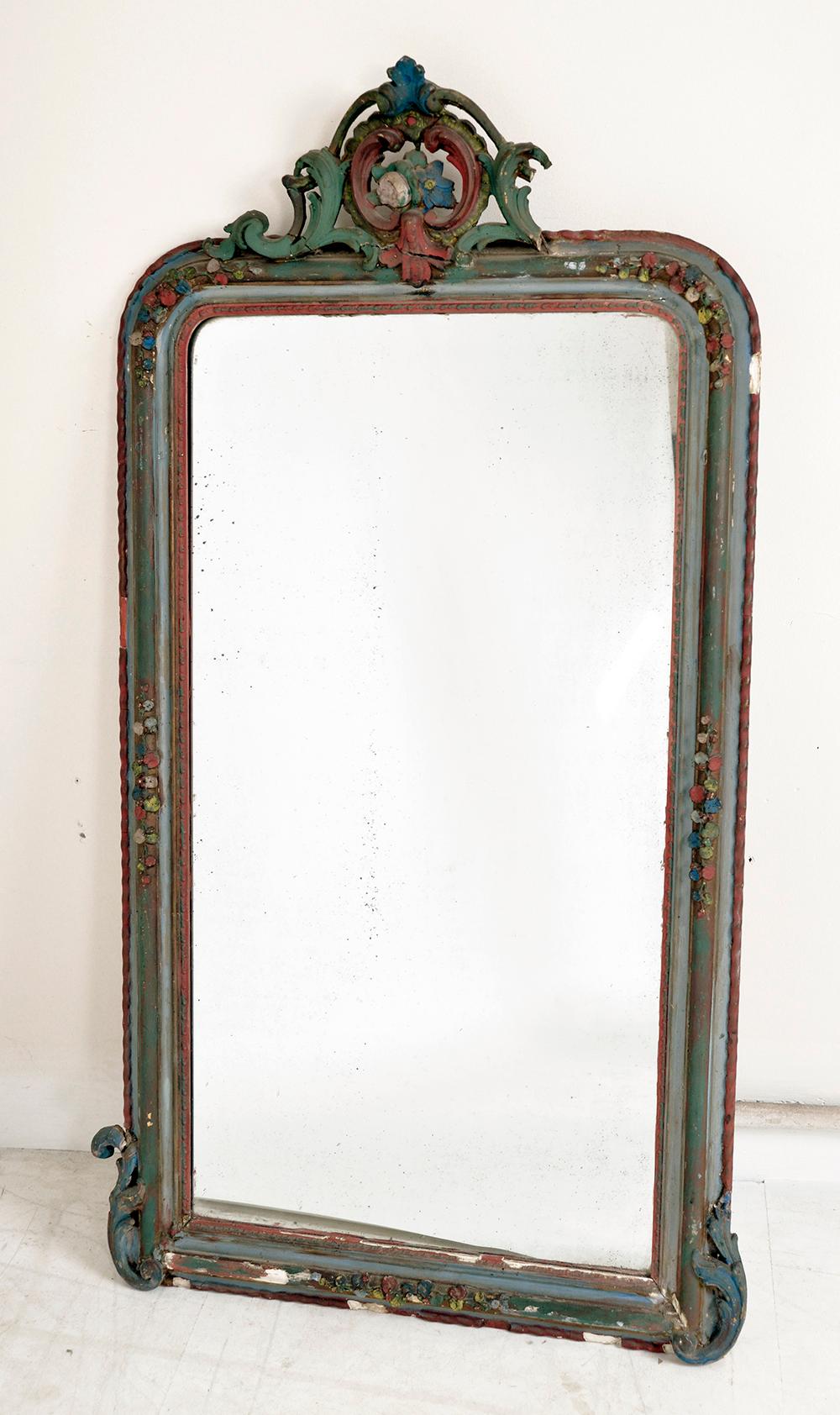 A very elegant late 19th century mirror bought in Belgium, featuring an elaborate wood and plasterwork surround with faded paint wood finish, and a desirable, lightly foxed glass mirror with a bright reflection. 
The floral crest is made from wire