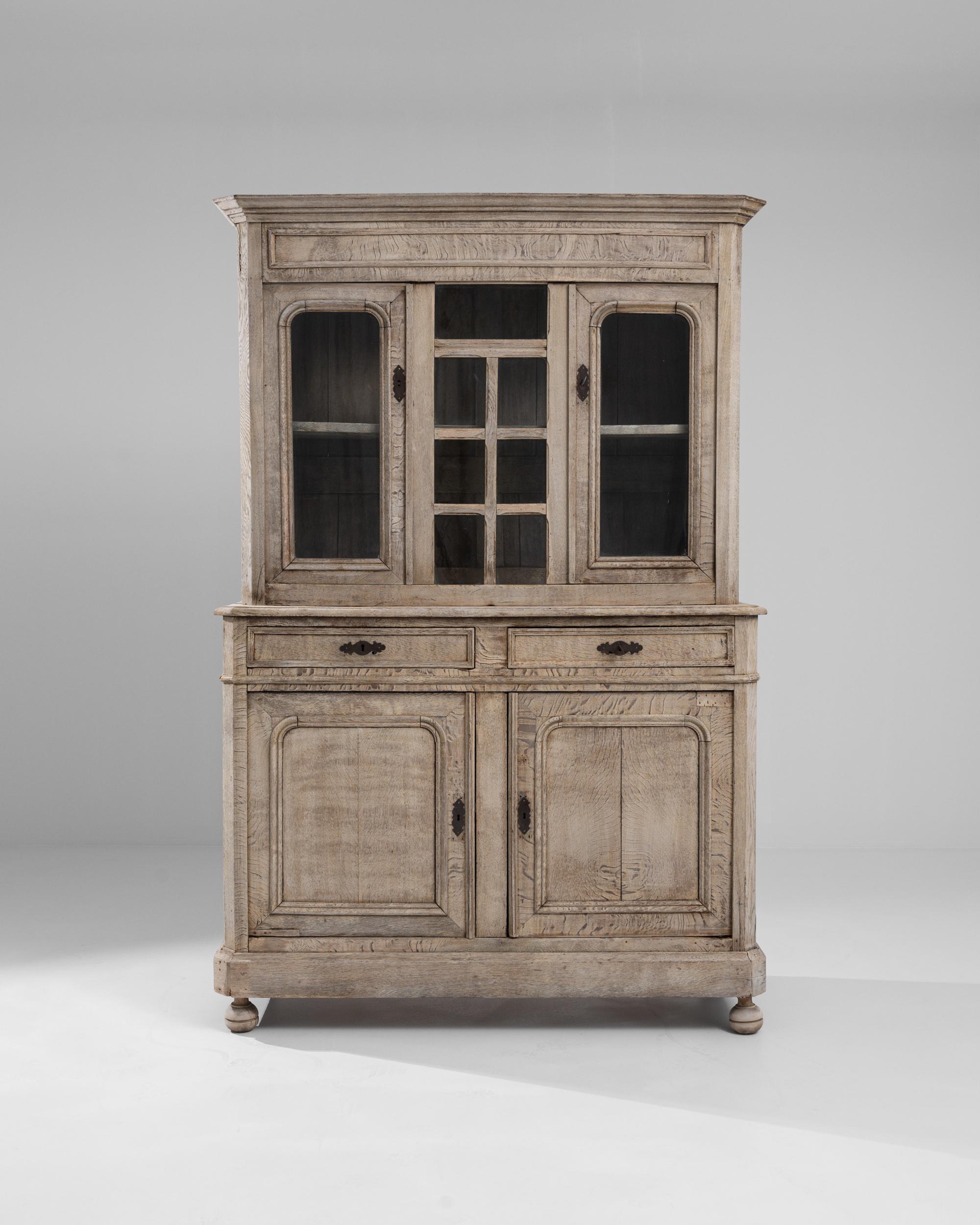 A wooden vitrine from 19th century Belgium. Fit with two upper display cabinets and two lower storage compartments, drawers slide in between, this vitrine boasts elegant design and is brimming with function. Its natural, wood grain-striped surface