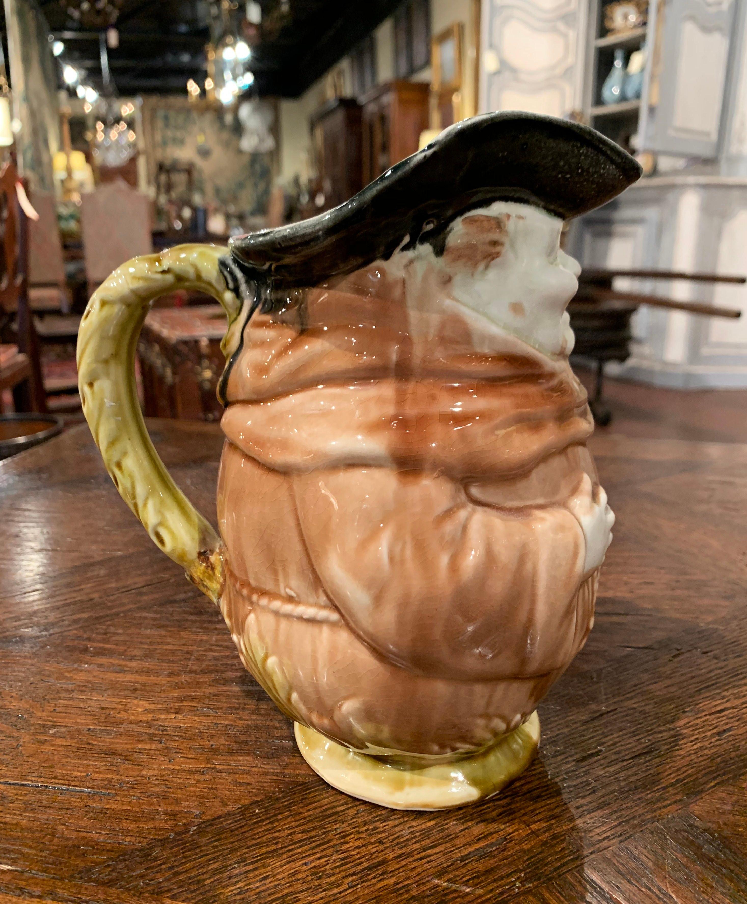 Decorate a wet bar with this charming, sculptural Majolica pitcher; crafted by Onnaing circa 1890, the antique, barbotine jug features a smiling monk with his hands on his chest in a greeting pose. The body and handle are hand painted in a brown