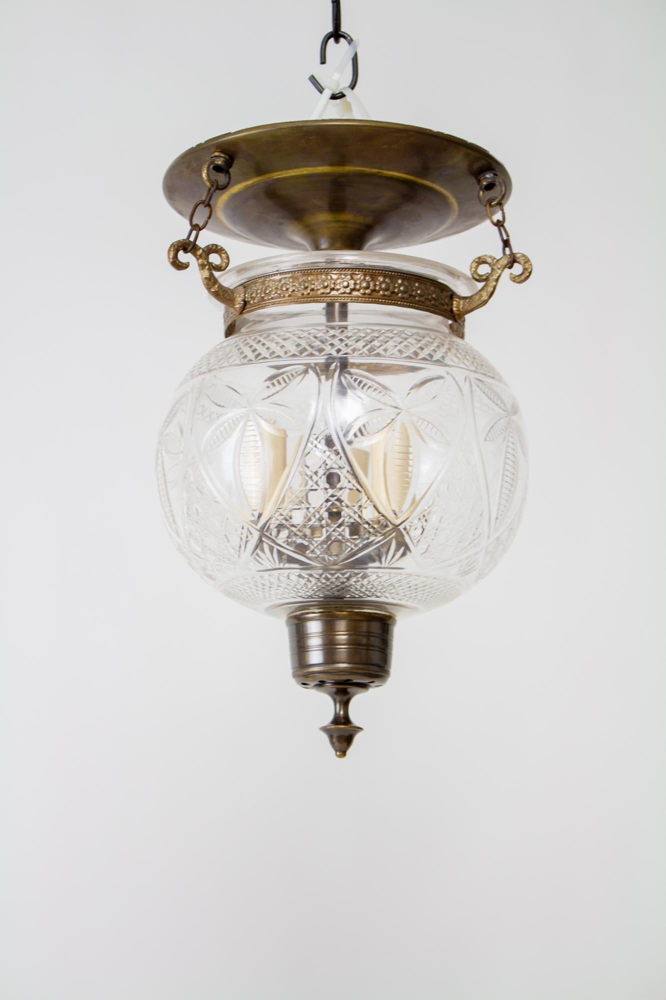 Bell jar lanterns first reached popularity in colonial India and due to their lingering popularity, production has continued to the present. Made from delicately blown clear glass with an engraved crosshatch and leaf pattern. The Glass is suspended