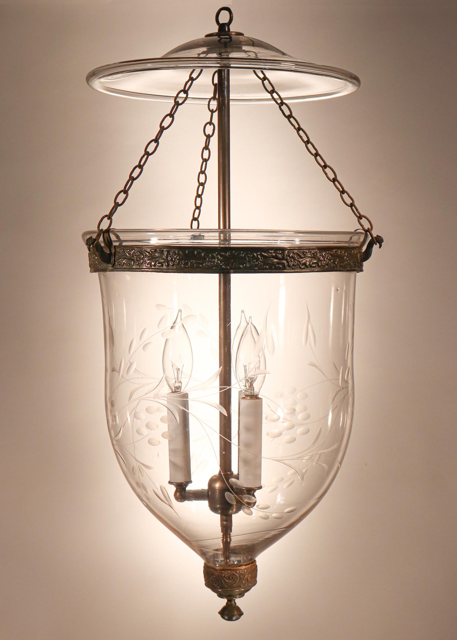 An exquisite antique English bell jar lantern with superb quality hand blown glass and a flowing, etched vine motif. This circa 1850 lantern features its original embossed brass band and brass finial/candleholder base (see photo detail). In