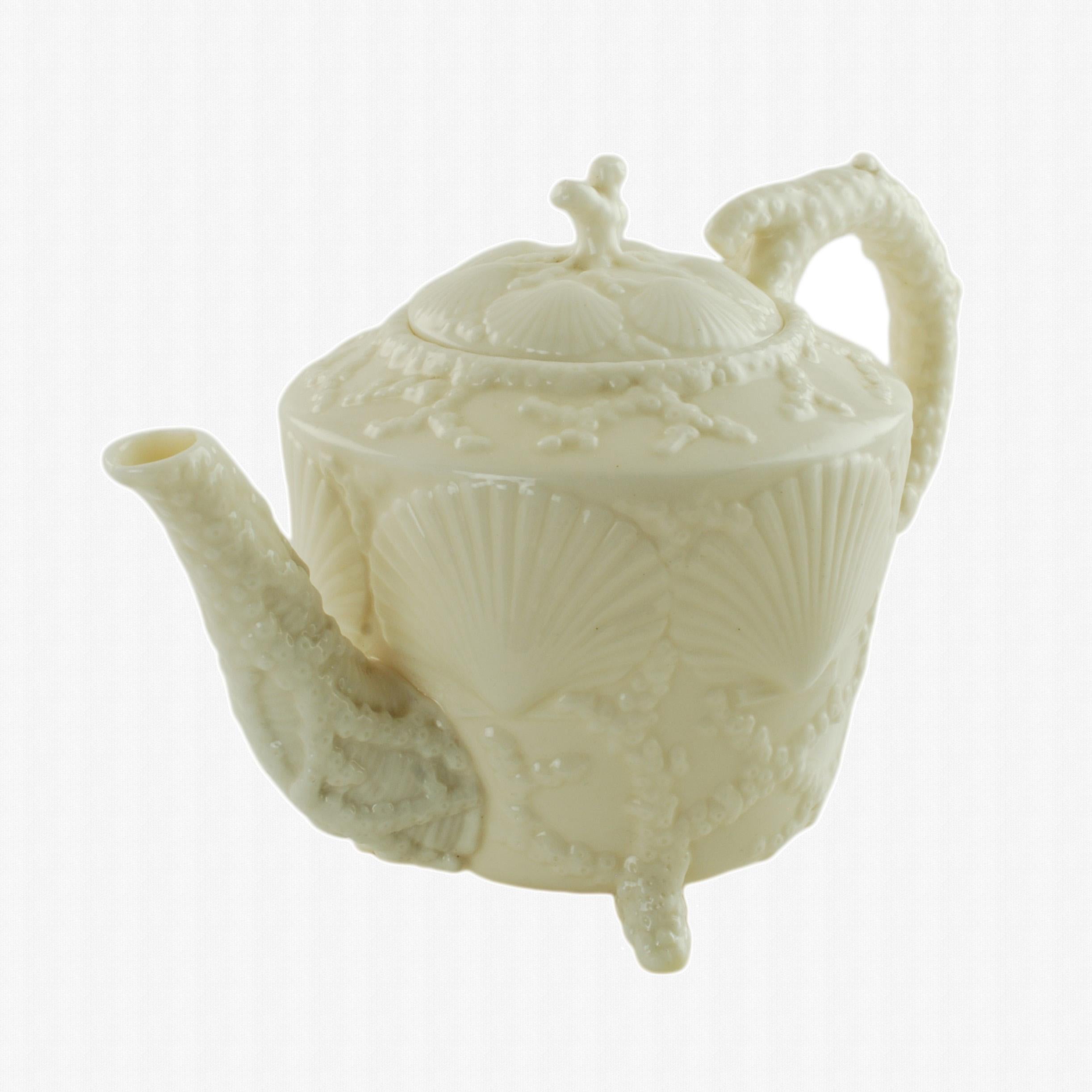 This rare late 19th century footed porcelain teapot was made by Belleek of Ireland in the shell pattern. The lid and body of the piece feature a series of moulded relief scallop shells along with coral detail. The teapot's coral elements form its