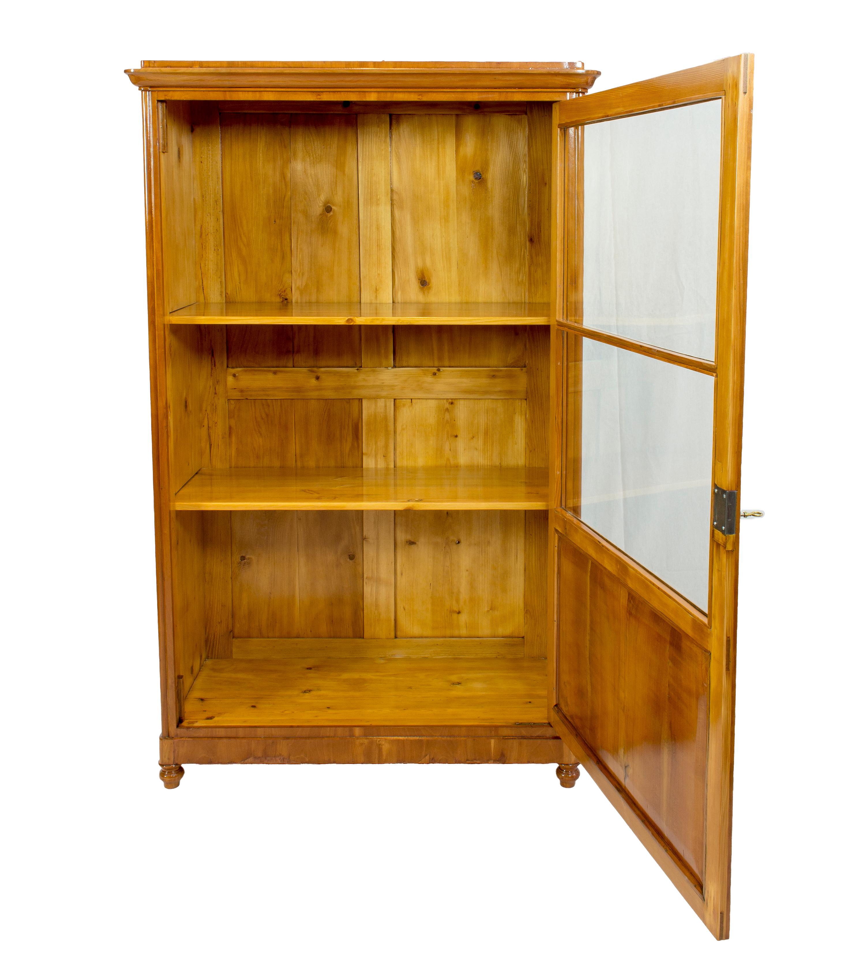 Beautiful one-door showcase cabinet, the body is made of pine wood with covered cherrywood veneer. The cabinet dates back to the Biedermeier period circa 1830. The glass is original mouth-blown from that period. In very good restored condition.