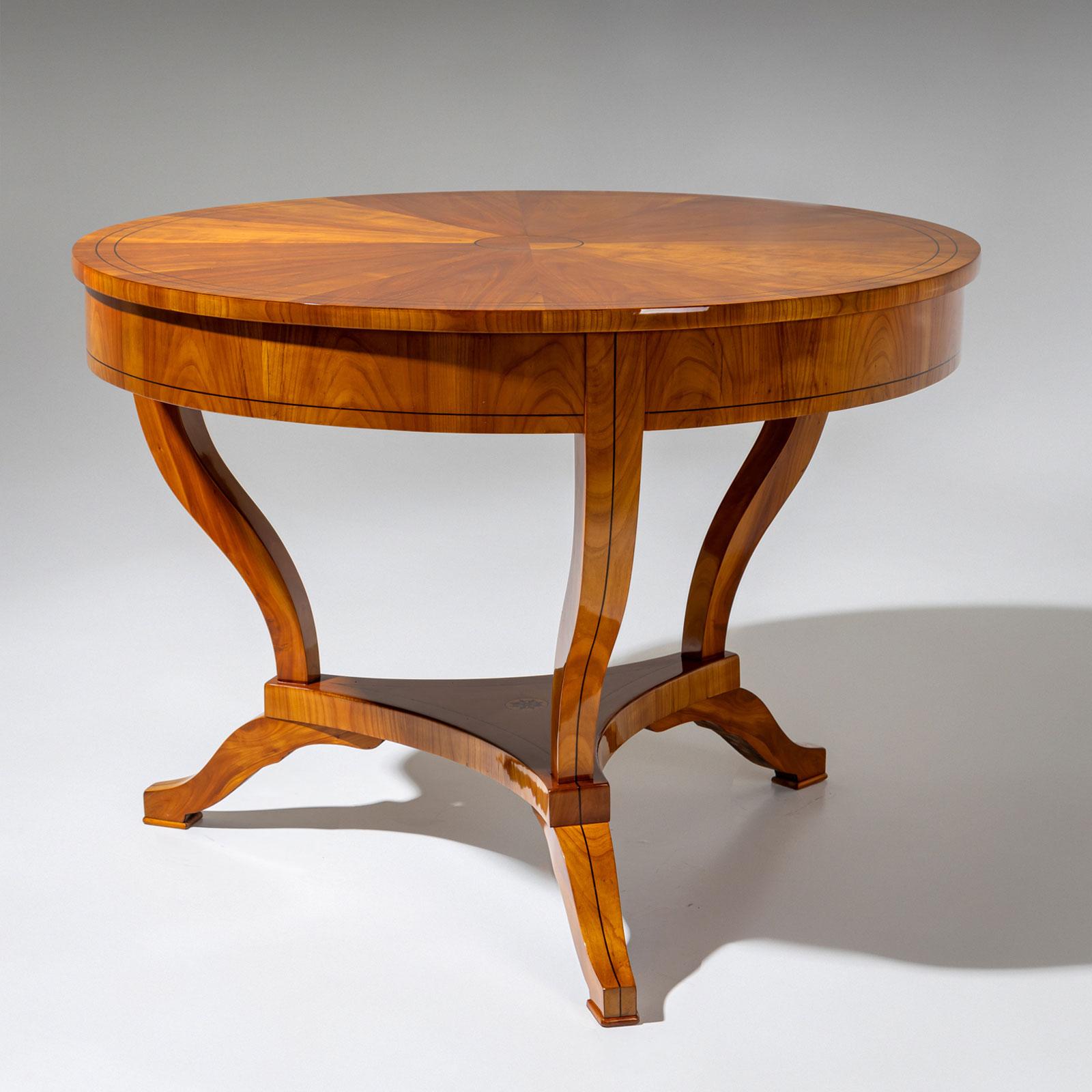 Runder Biedermeier-Tisch auf drei Beinen mit dreifachem Mittelbrett und glatter Zarge. Die Tischplatte ist radial furniert und in der Mitte mit kreisförmigen Fadenintarsien verziert. Die Fadenintarsien setzen sich elegant an den Beinen und der Zarge