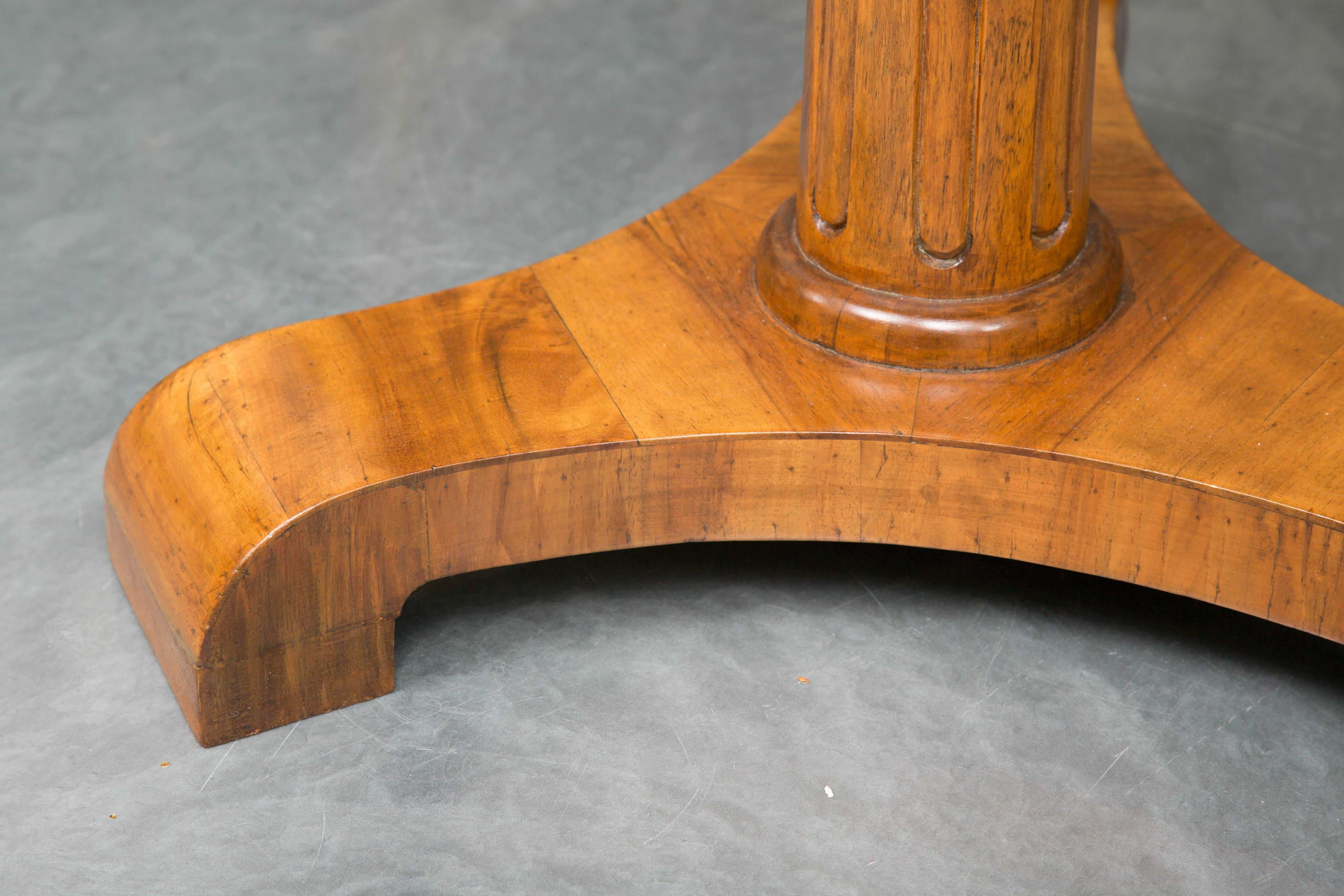 This is a very pleasant Biedermeier cherrywood circular table. The top is designed with pie-slice veneer with a notched wood frieze supported by a round tapering fluted pedestal situated on a tripartite plinth, circa 1830.