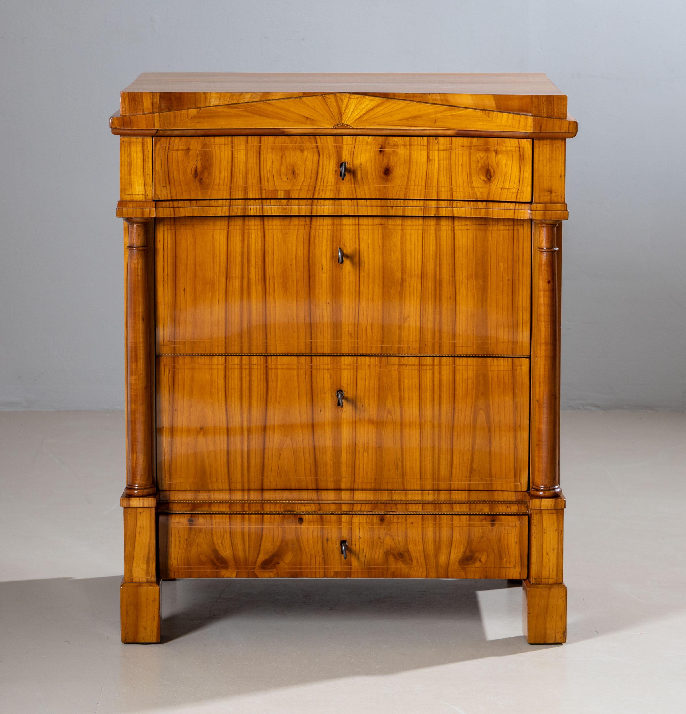 Elegant Biedermeier chest of drawers featuring four drawers and a distinctive pediment-shaped front, flanked by lateral half-columns. The top drawer slightly projects and rests on finely crafted capitals. Veneered in beautiful cherrywood and inlaid