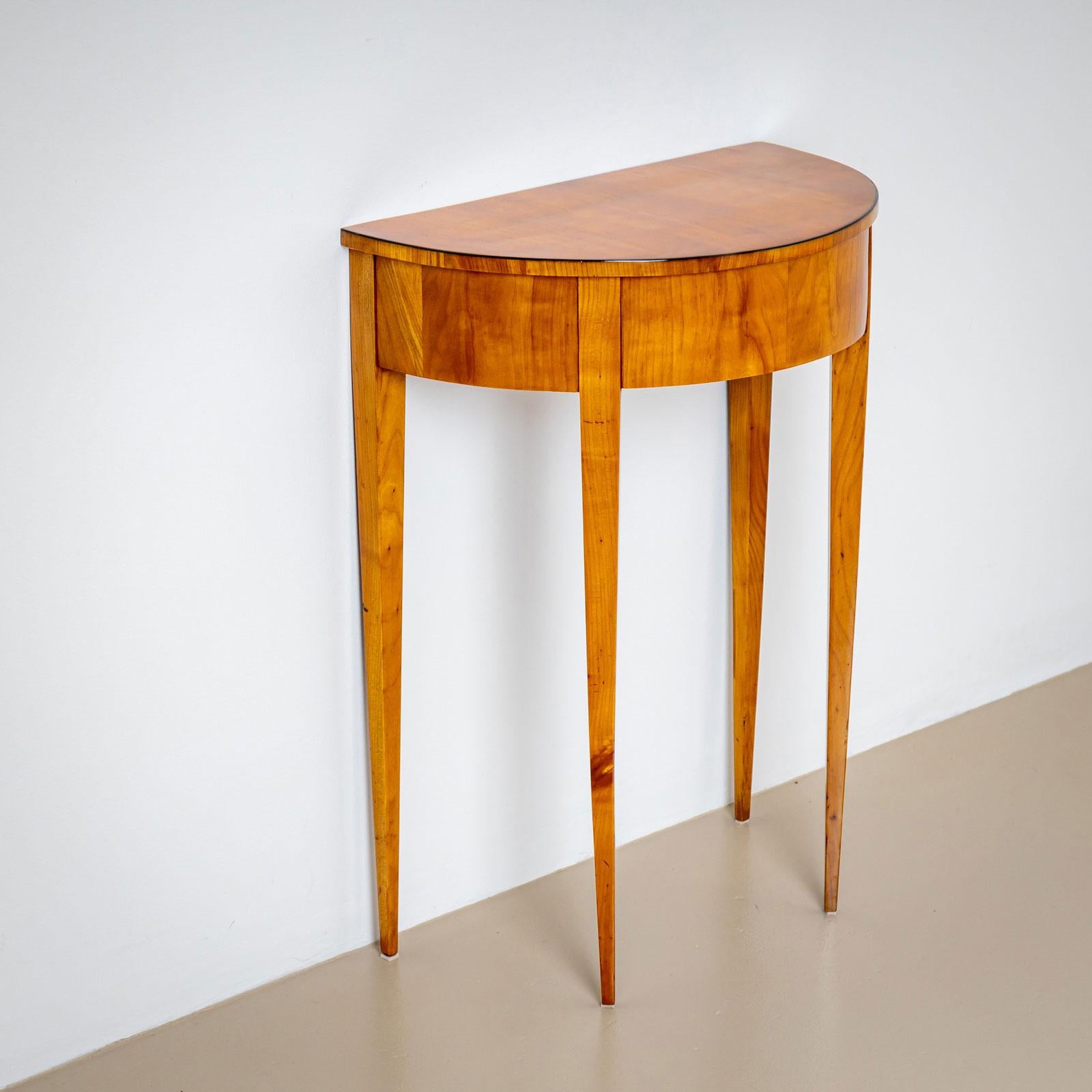 Biedermeier Demi Lune console table in cherry with one drawer on tall tapering legs. The top edge of the table top is ebonized. The console has been professionally restored and hand polished with shellac.