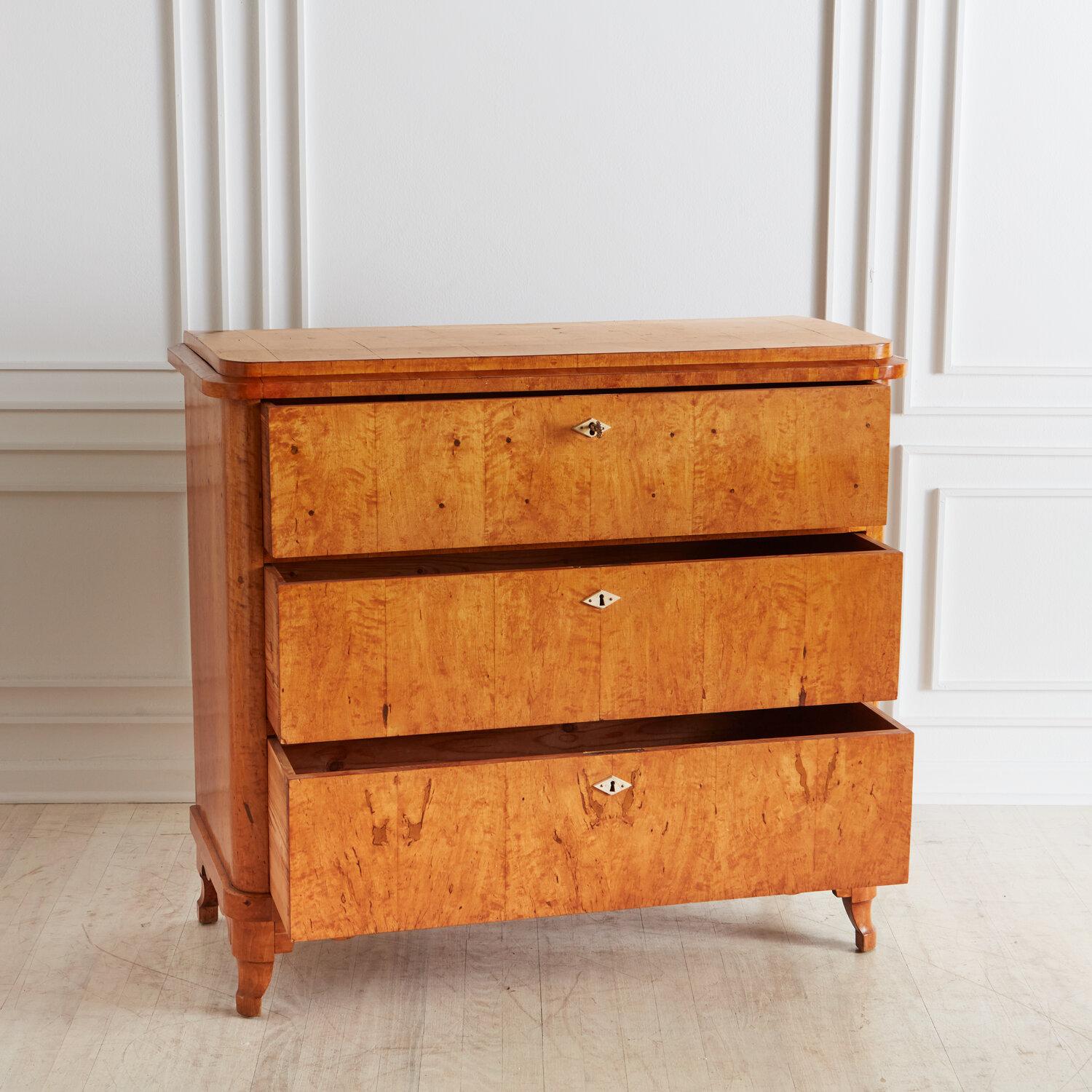 A 19th century chest of three drawers in the Biedermeier style; featuring three drawers each with a lock that a single key (included) can lock or unlock. The key is used to open the drawers. Nested inside the top drawers are four smaller jewelry