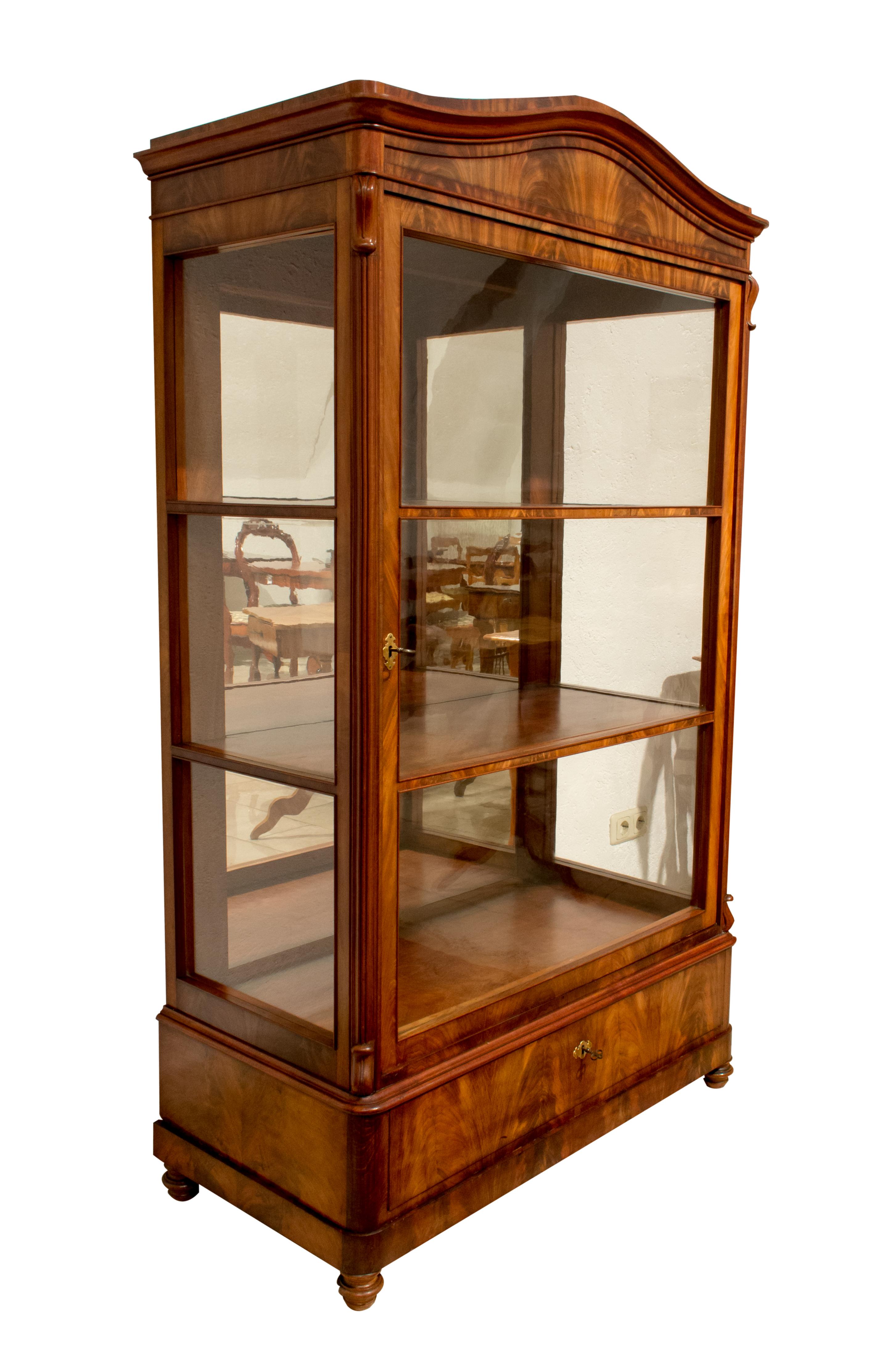 Very nice three-sided showcase with a continuous veneer picture of mahogany. The top is also veneered. The display case dates from the time of the late Biedermeier period (Louis Philippe), circa 1845. The glasses are all original from the time.